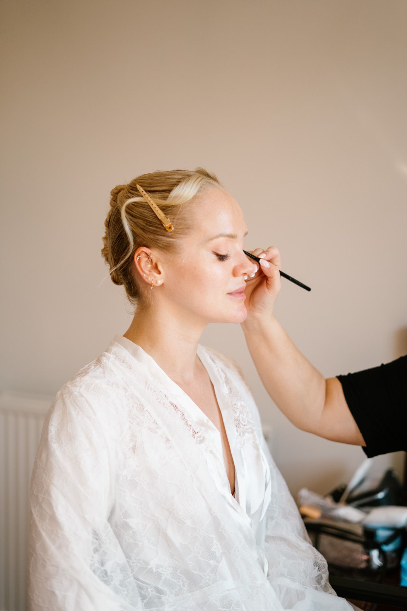 Makeup application in progress with white silk robe during wedding preparations.