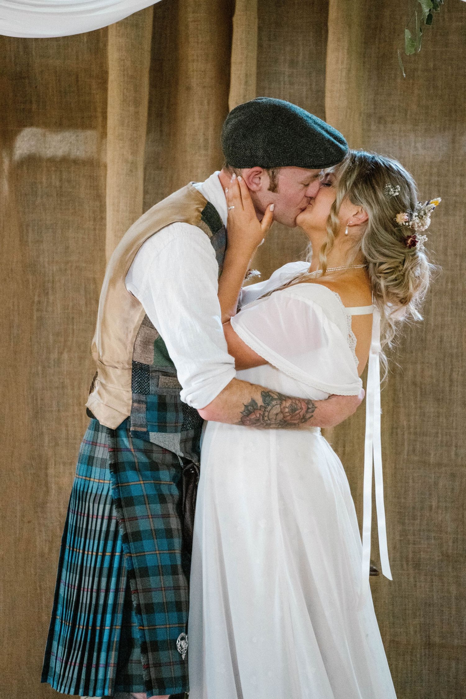 A romantic first kiss moment at a rustic wedding ceremony.
