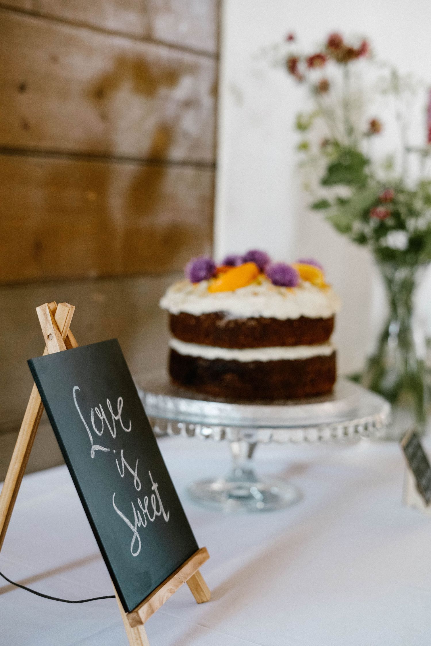 A rustic chocolate layer cake with edible flowers displayed on a crystal cake stand.