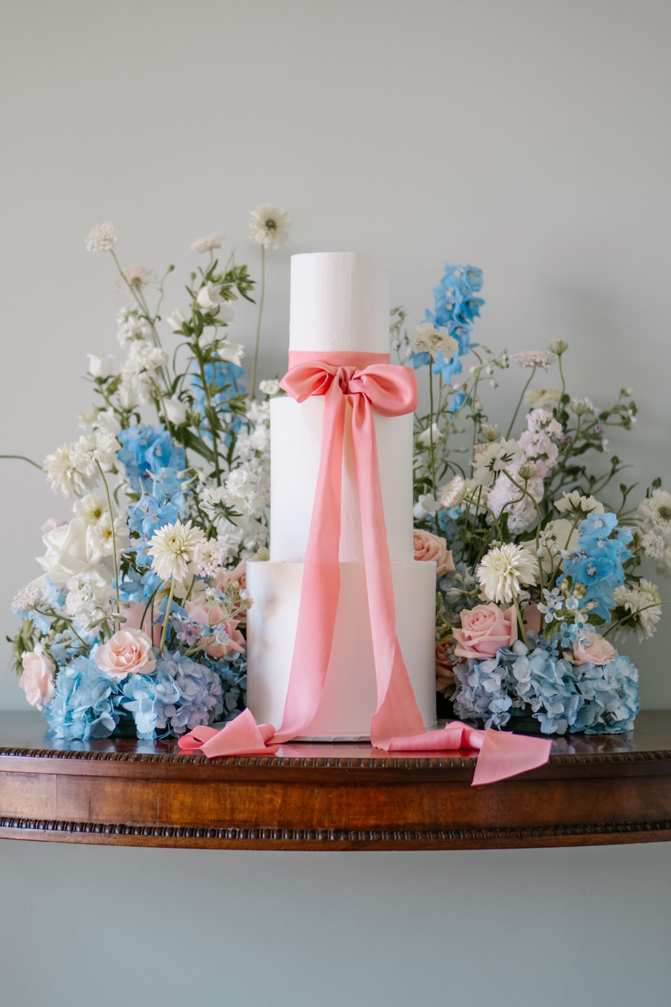 Wedding decor featuring white and blue hydrangeas with pink ribbons on wooden shelf.