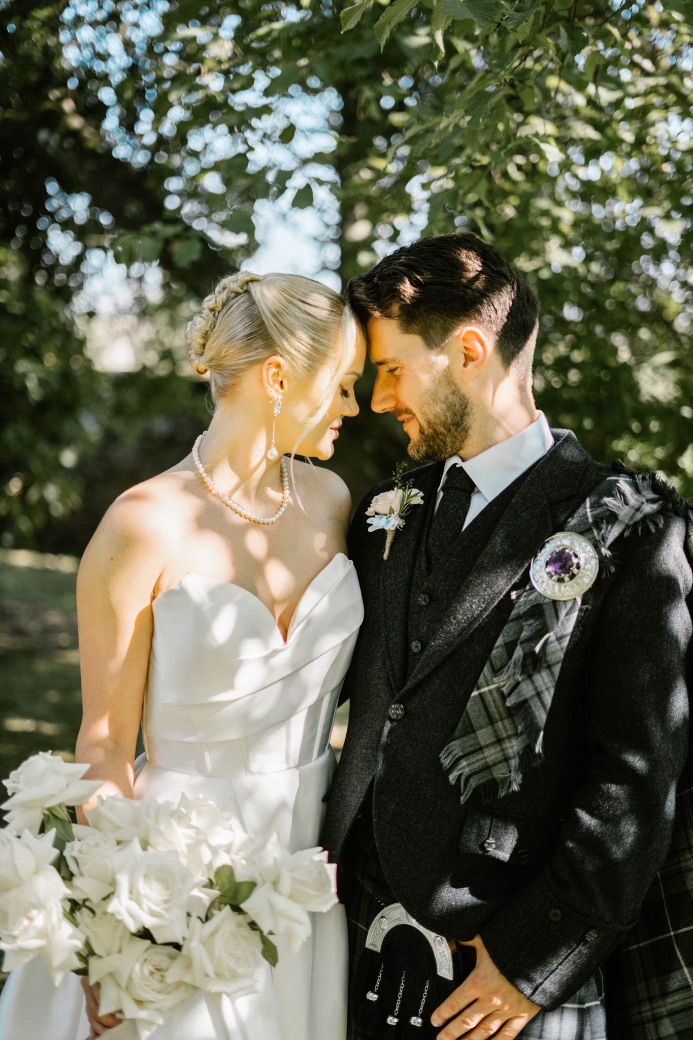 A romantic wedding portrait in dappled sunlight with Scottish formal attire.