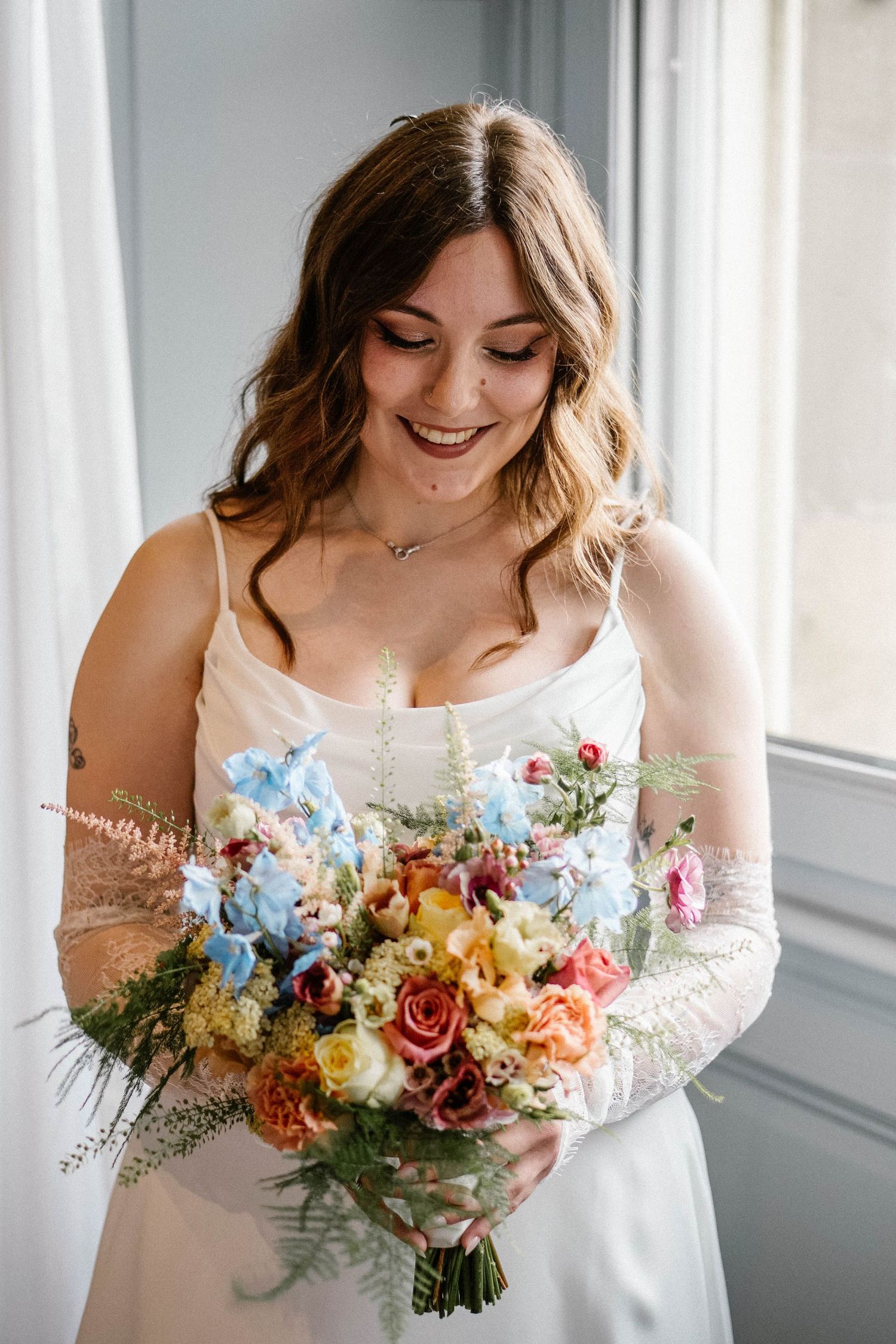 Bride holding a vibrant bouquet of mixed flowers in peach, yellow and coral tones.