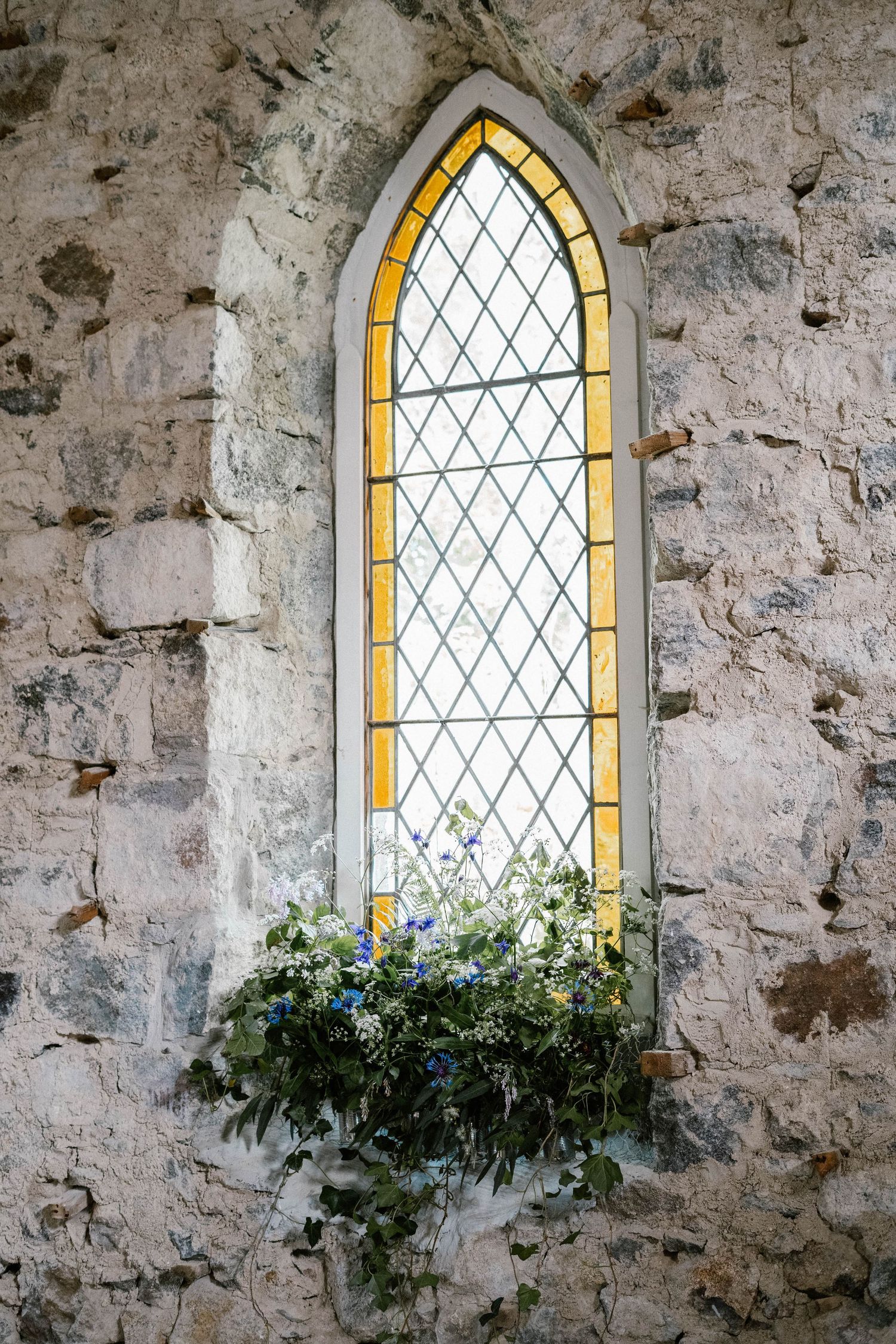 Gothic arched church window with yellow stained glass and greenery decorations.