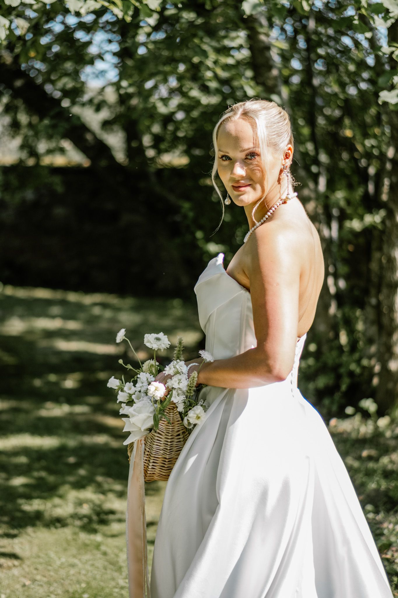 White wedding dress flowing in sunlit garden setting.