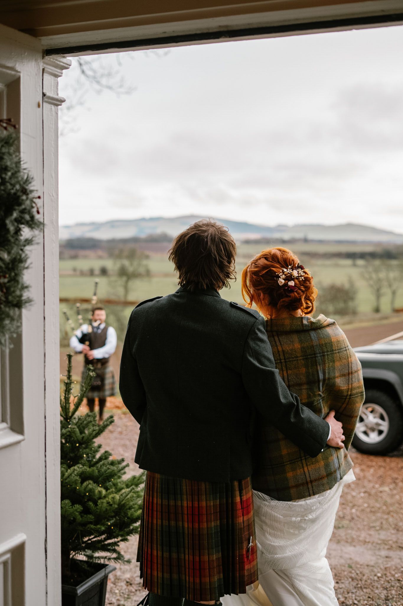 Couple in traditional Scottish attire looking out over a scenic countryside landscape.
