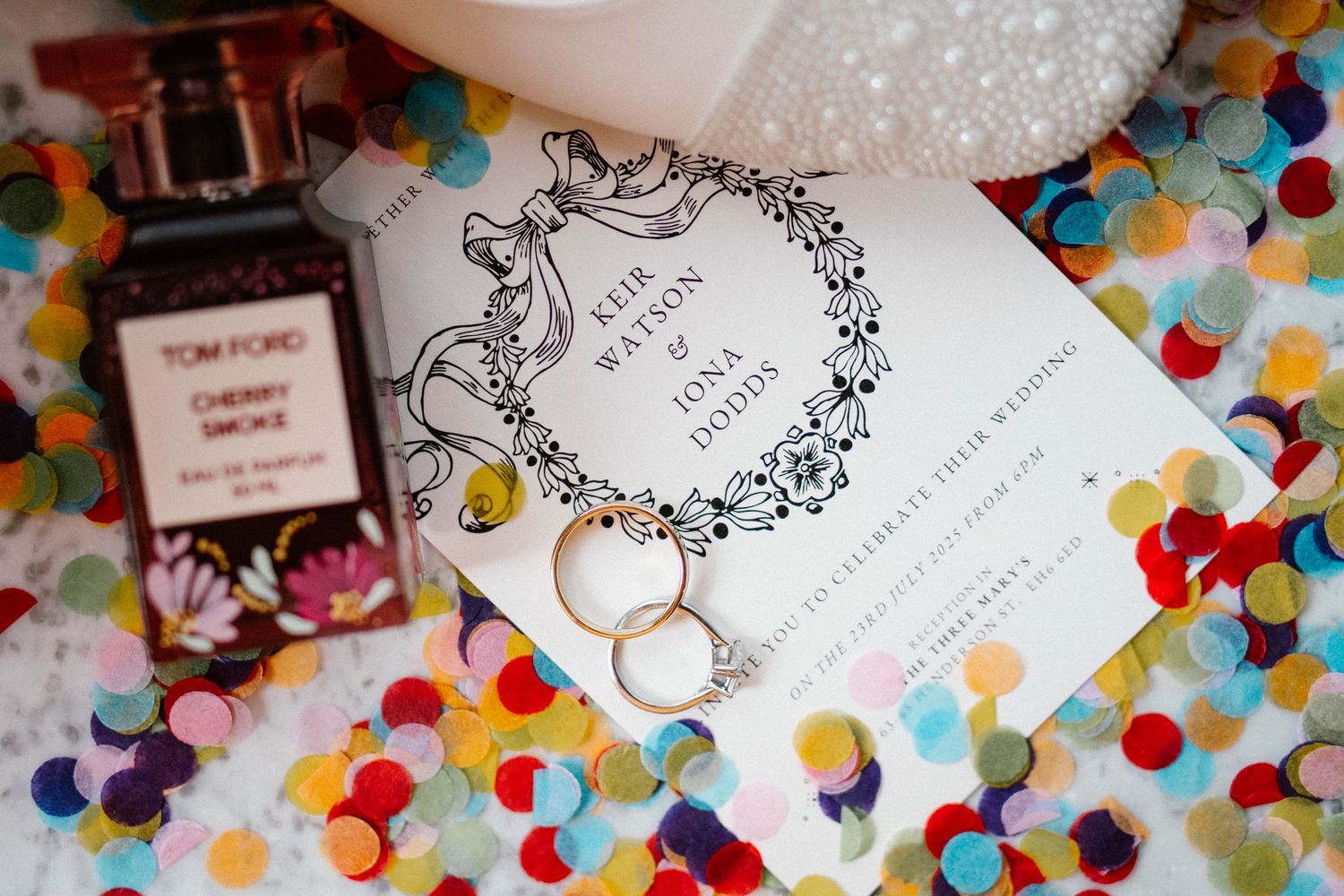 Wedding invitations and rings displayed on a colorful confetti background.
