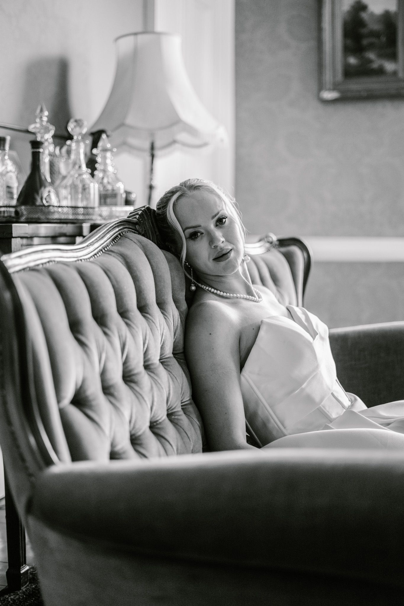 Bride reclining on vintage tufted couch in black and white photography.