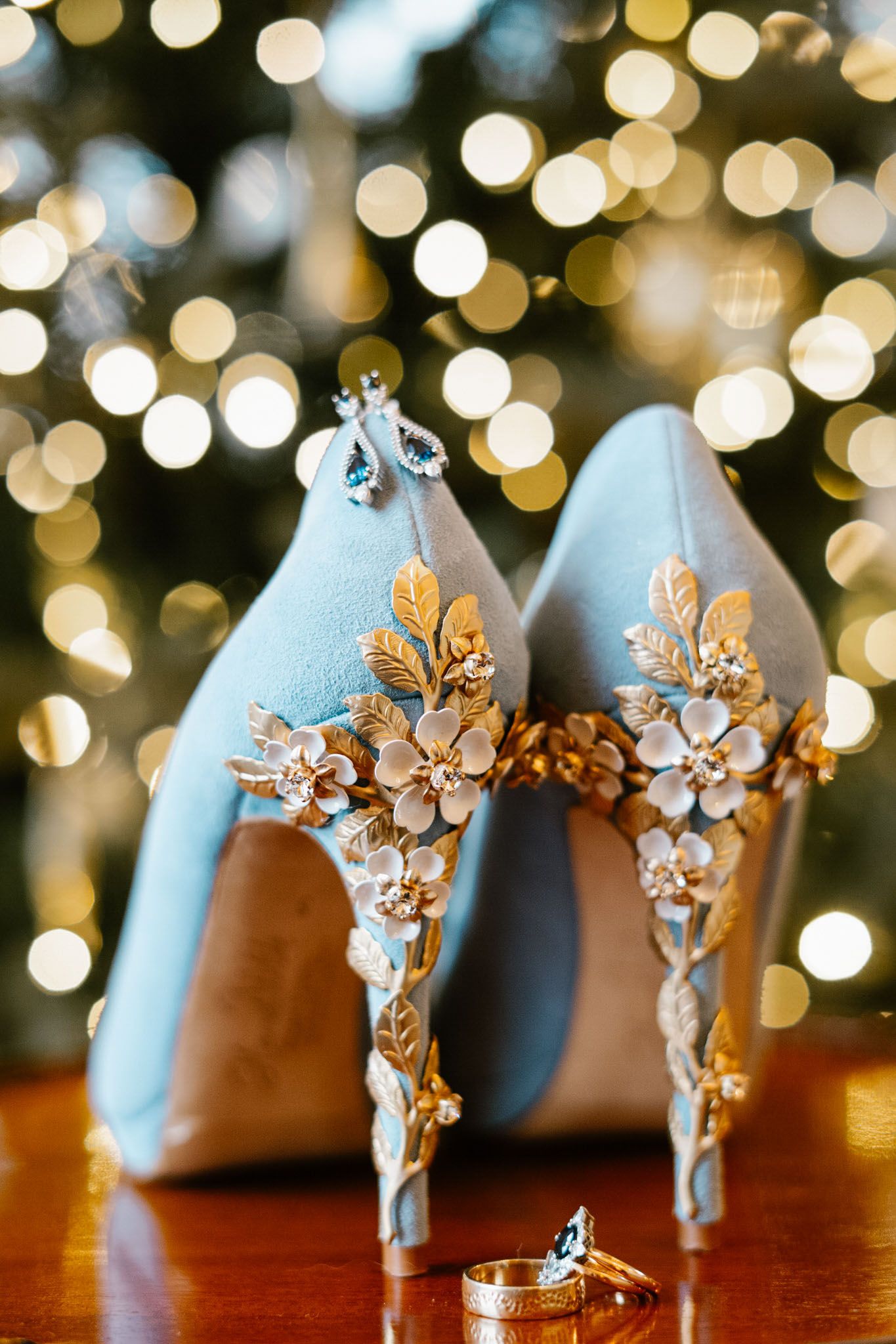Light blue wedding shoes with ornate gold floral details against bokeh light background.