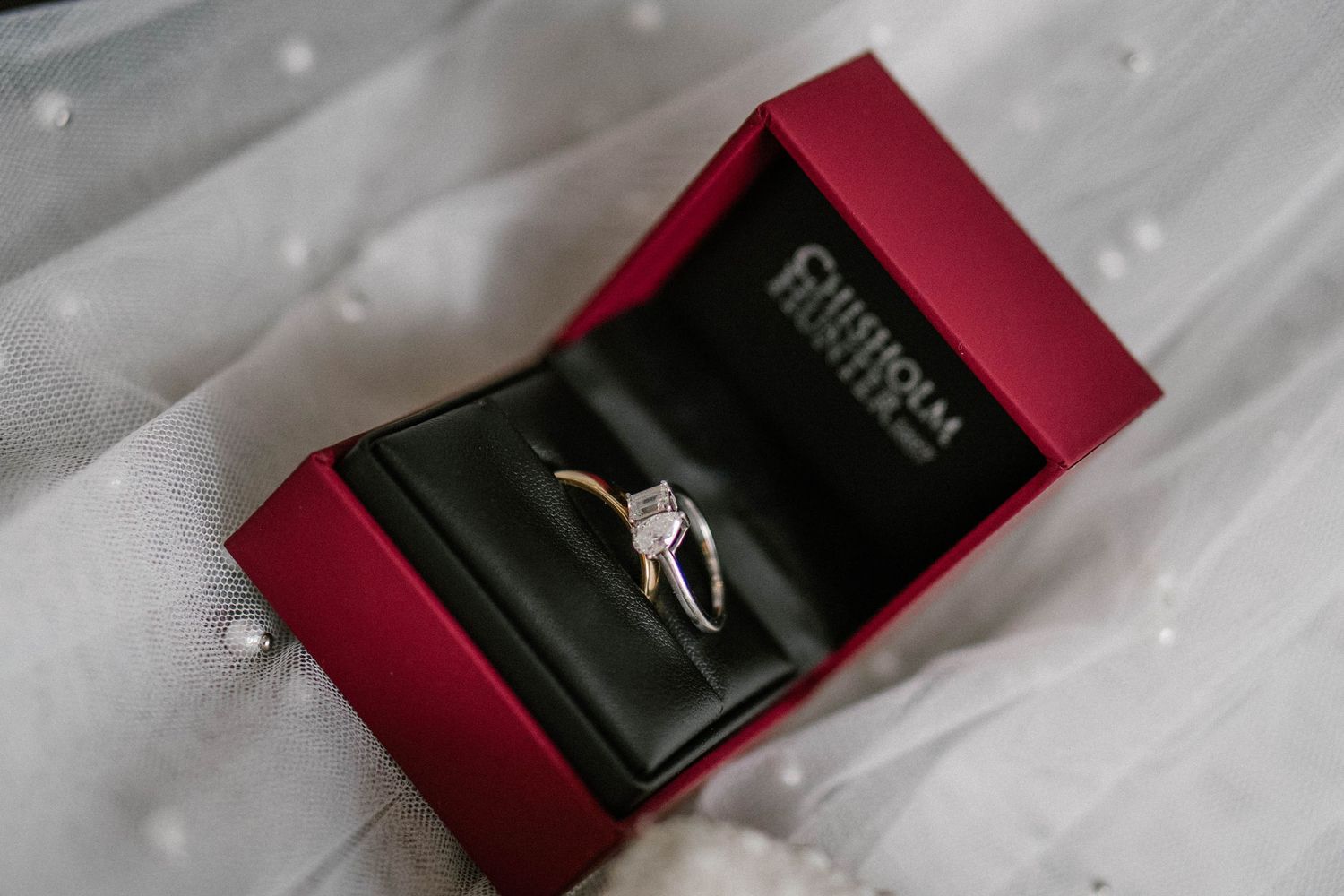 Wedding rings displayed in elegant burgundy ring boxes on white fabric.