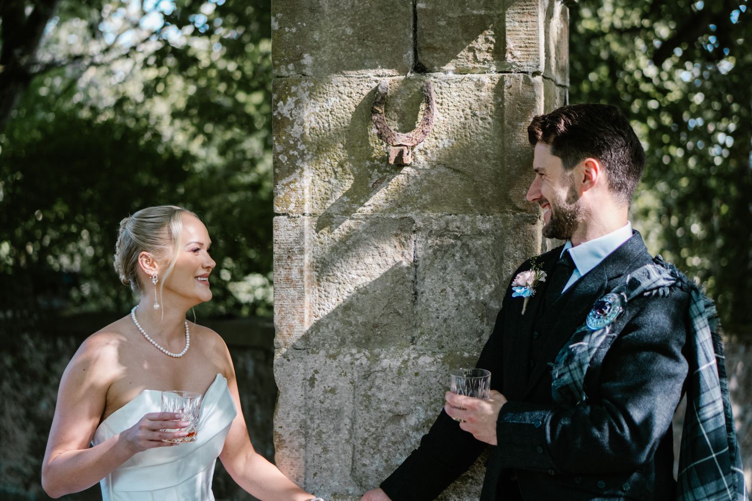 Wedding couple sharing intimate moment against stone wall in garden setting.