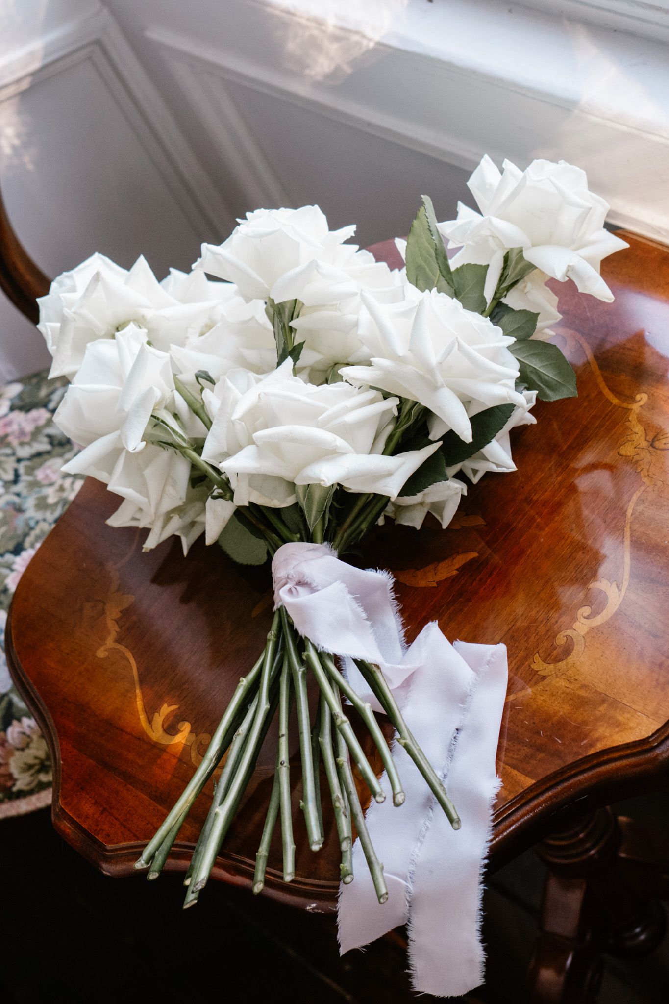 A beautiful bouquet of white roses tied with ribbon on a polished wooden surface.