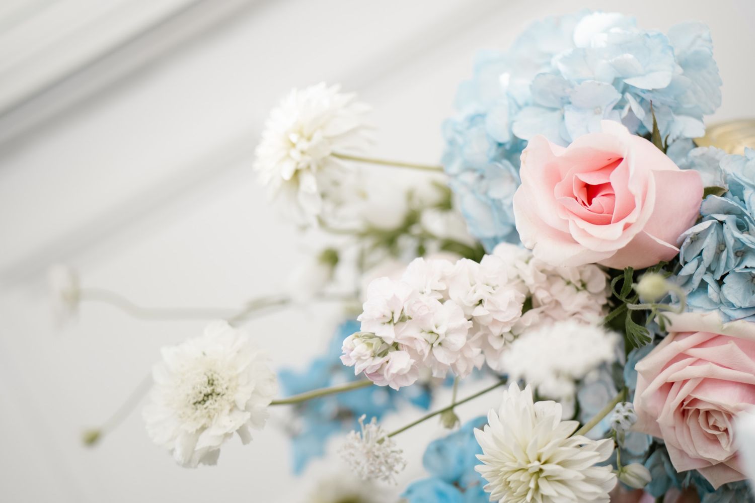 Delicate arrangement of blue hydrangeas and pink roses with soft white flowers.