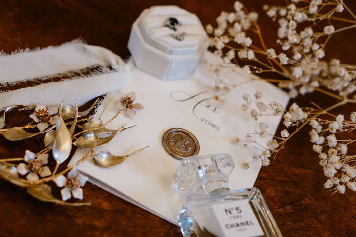 Wedding details with Chanel perfume, baby's breath flowers, and stationery on wooden surface.