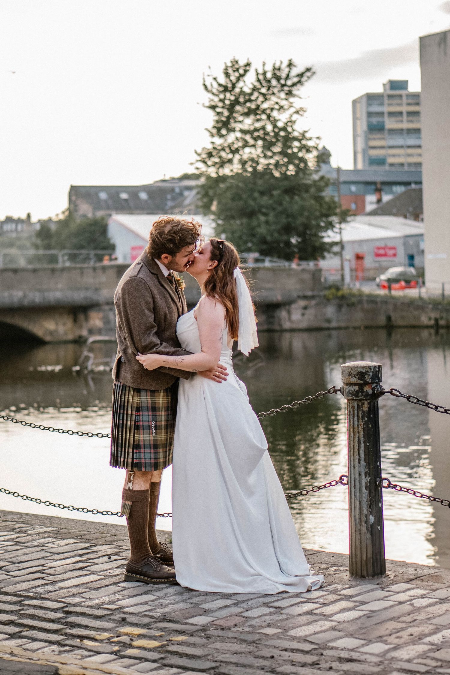 Romantic waterfront wedding photos with couple posing on cobblestone dock at sunset.