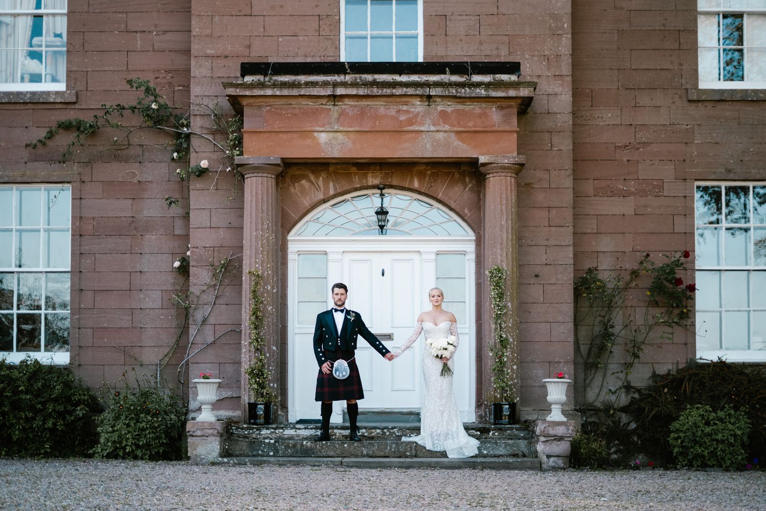 Wedding couple posing in front of grand stone building with classical architecture.