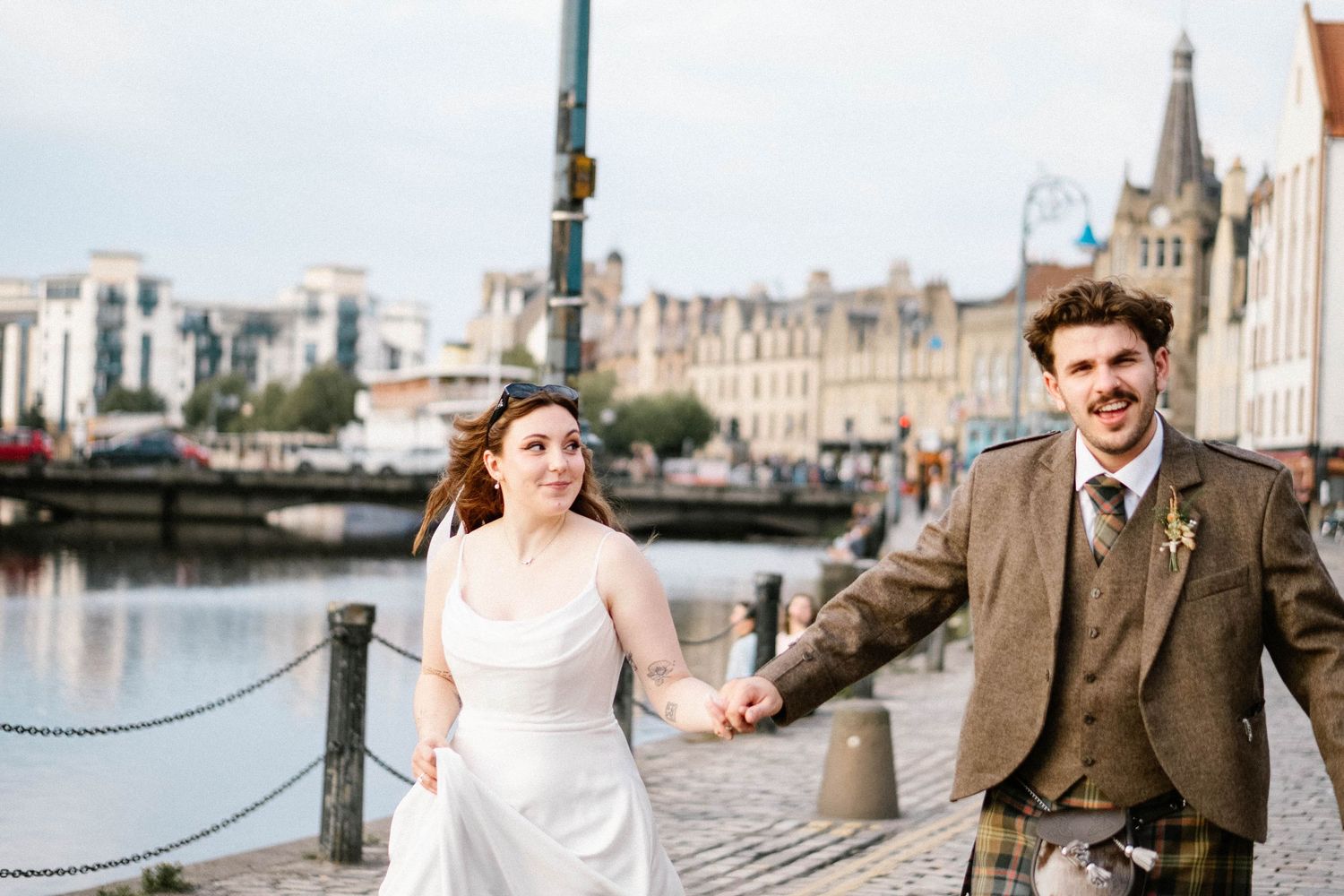 Wedding couple walking along historic waterfront with classic architecture in background.