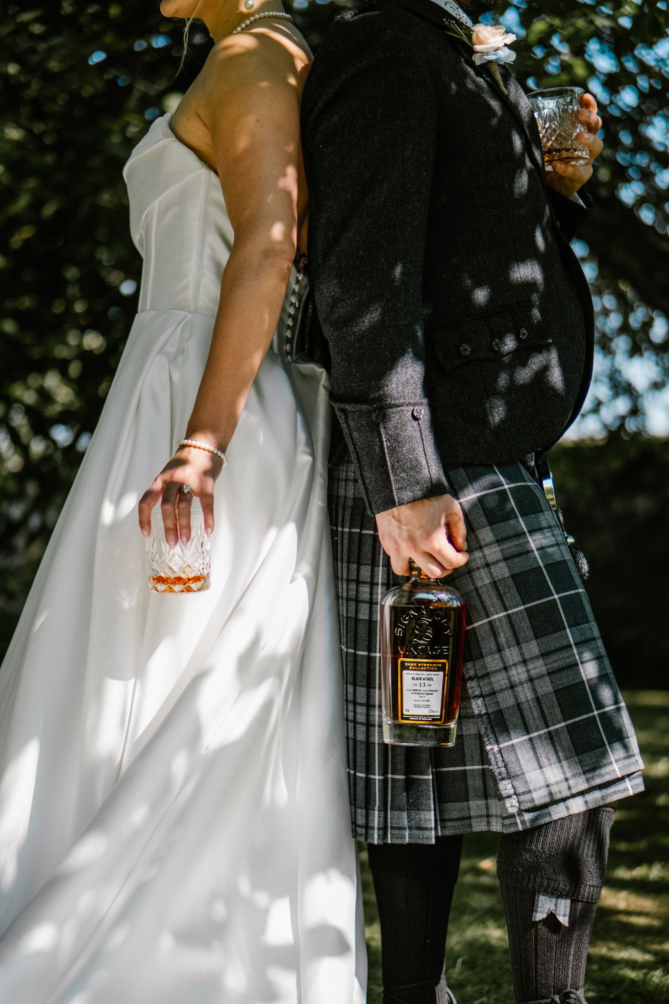 Close-up of bride and groom in traditional Scottish kilt holding hands outdoors.