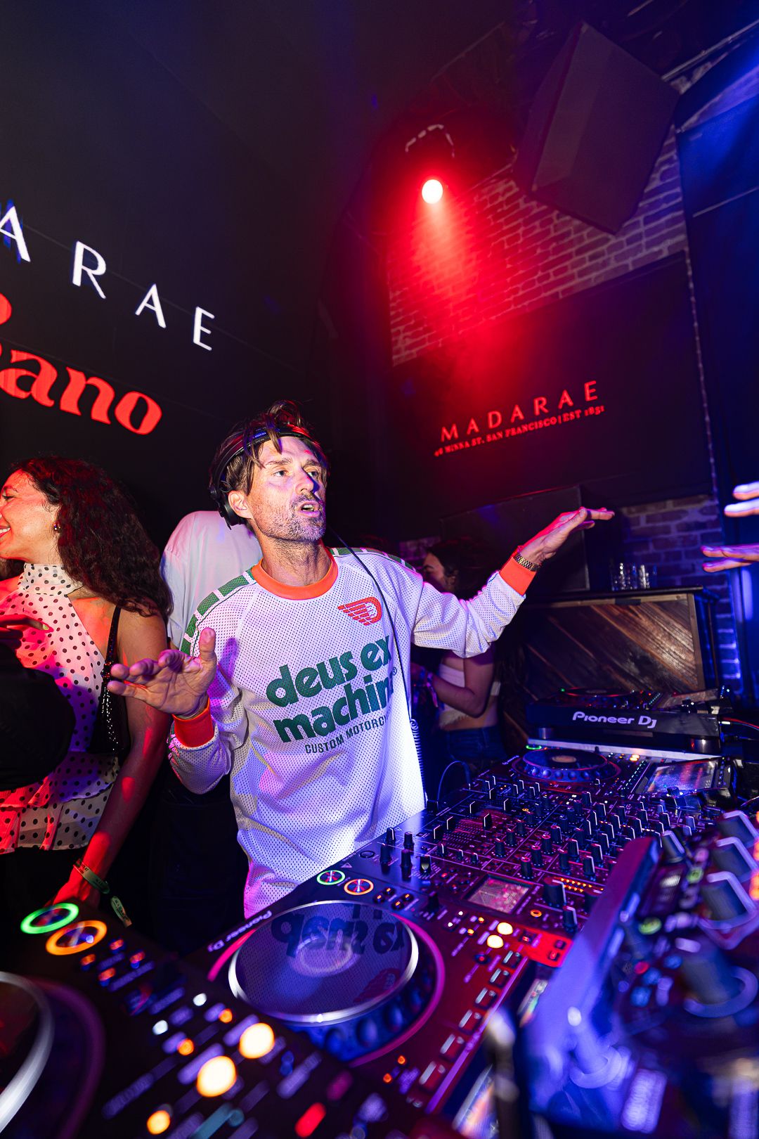 Energetic DJ performs at nightclub event with Pioneer DJ equipment under red stage lighting.
