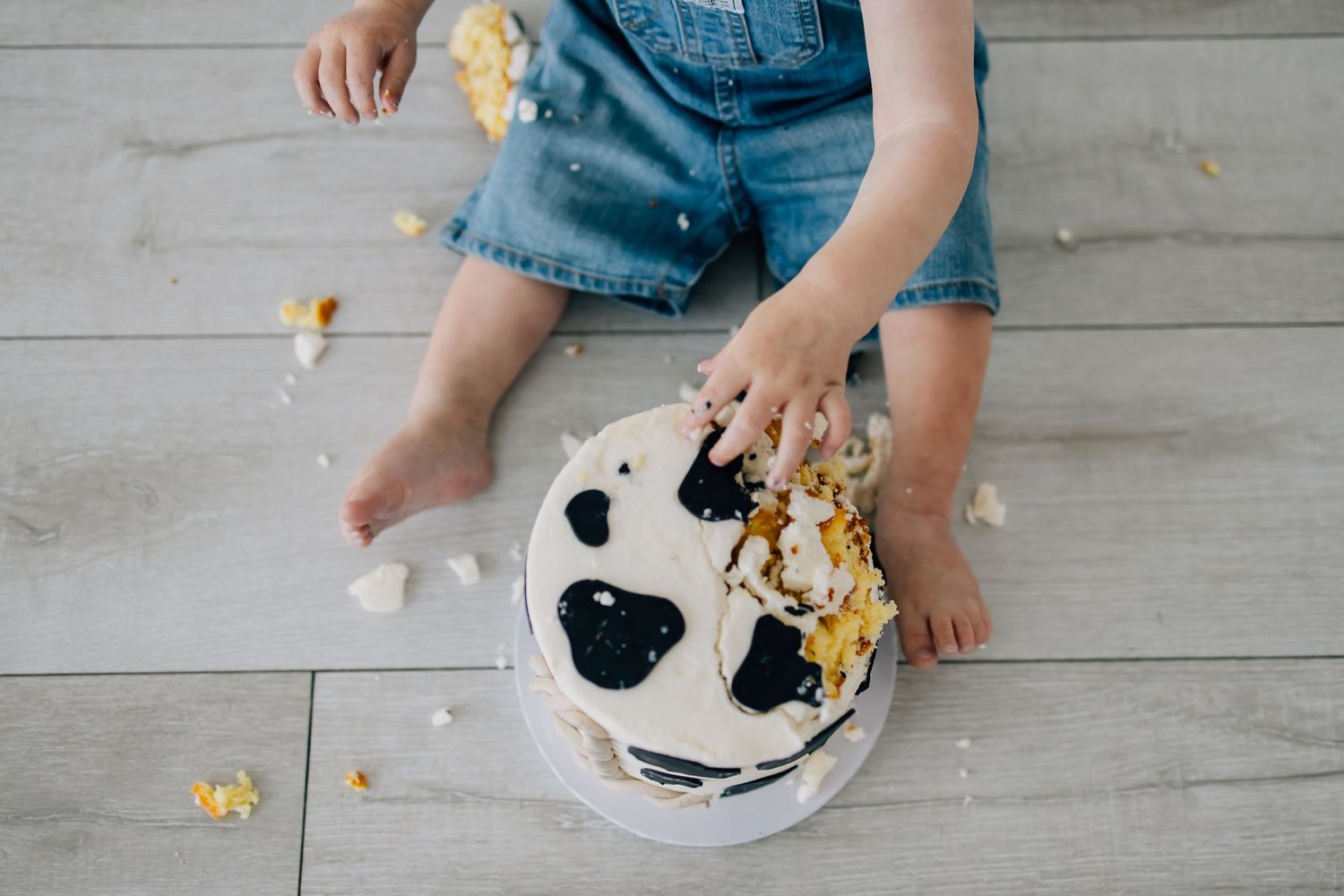 Photography of a small child in overalls reaching for a chunk of cake