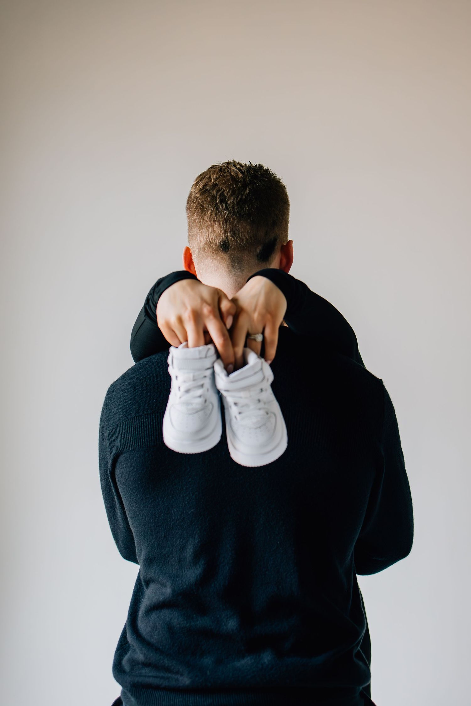 Maternity photography emphasizing new baby shoes being held by the mother in an embrace around the father-to-be