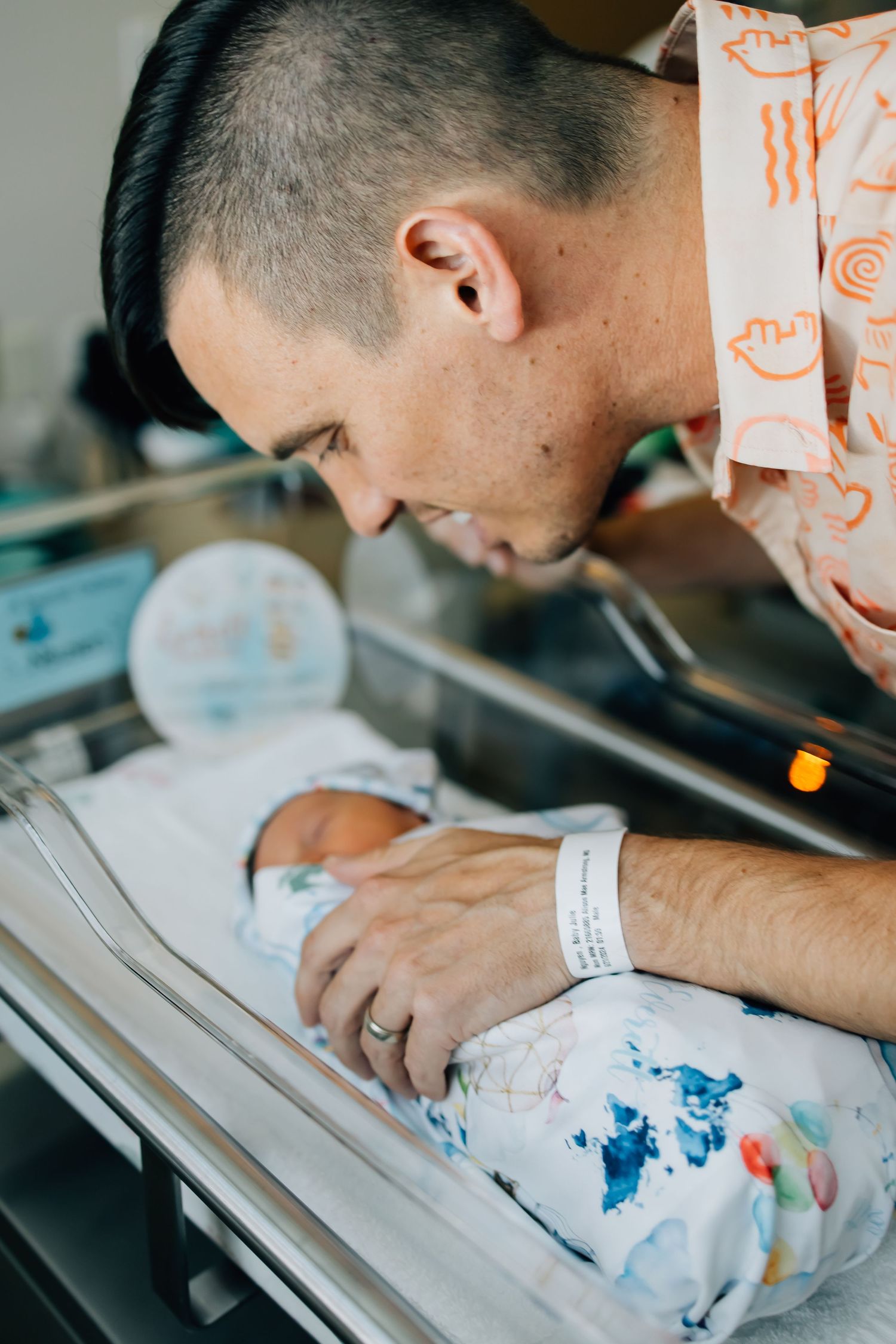 Portrait photography of a newborn in a hospital bassinet with father leaning over and smiling at infant
