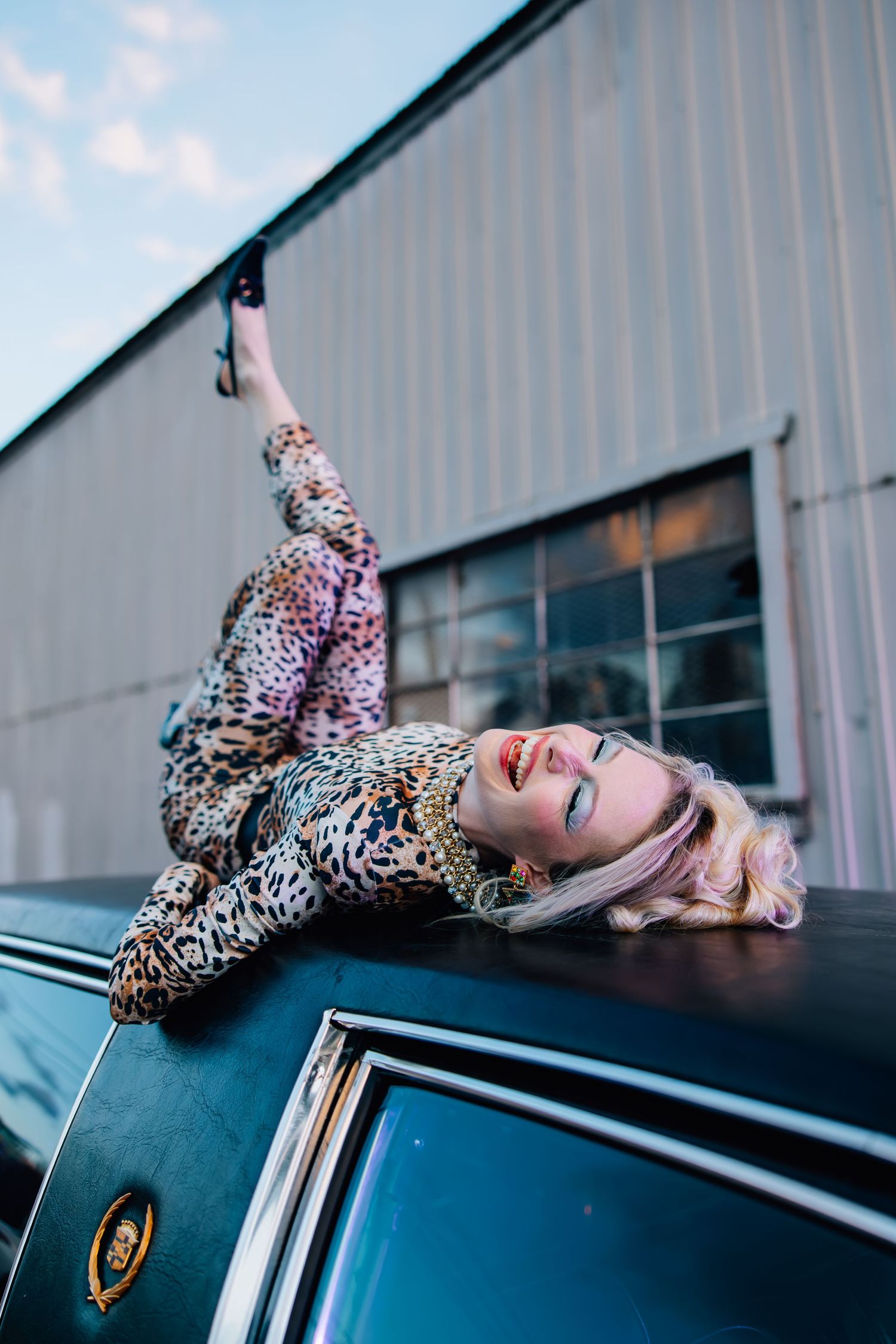 Editorial-style image featuring woman in 80s attire laying on top of a vintage limo