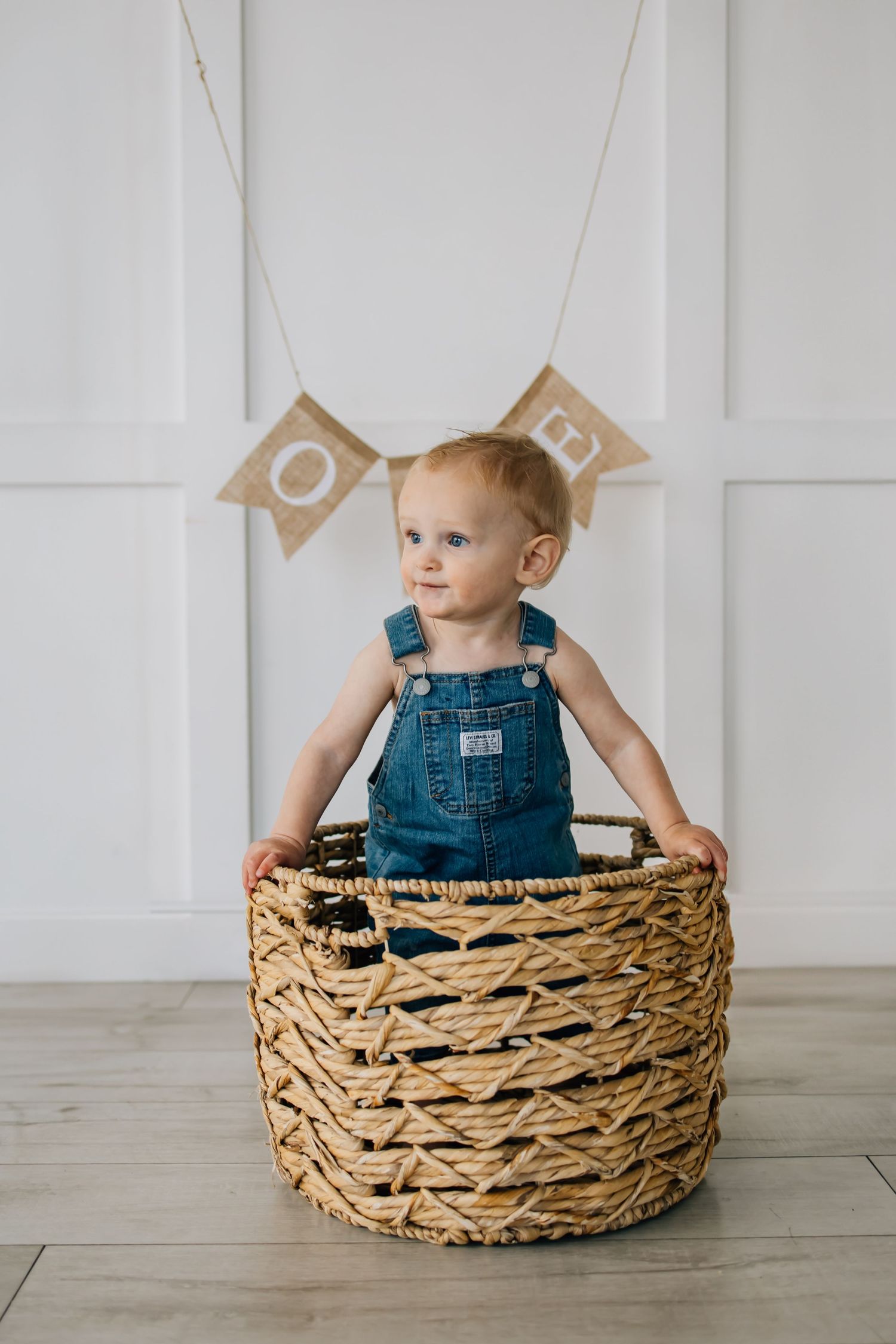 Portrait photography of a small child in overalls popping out of a basket