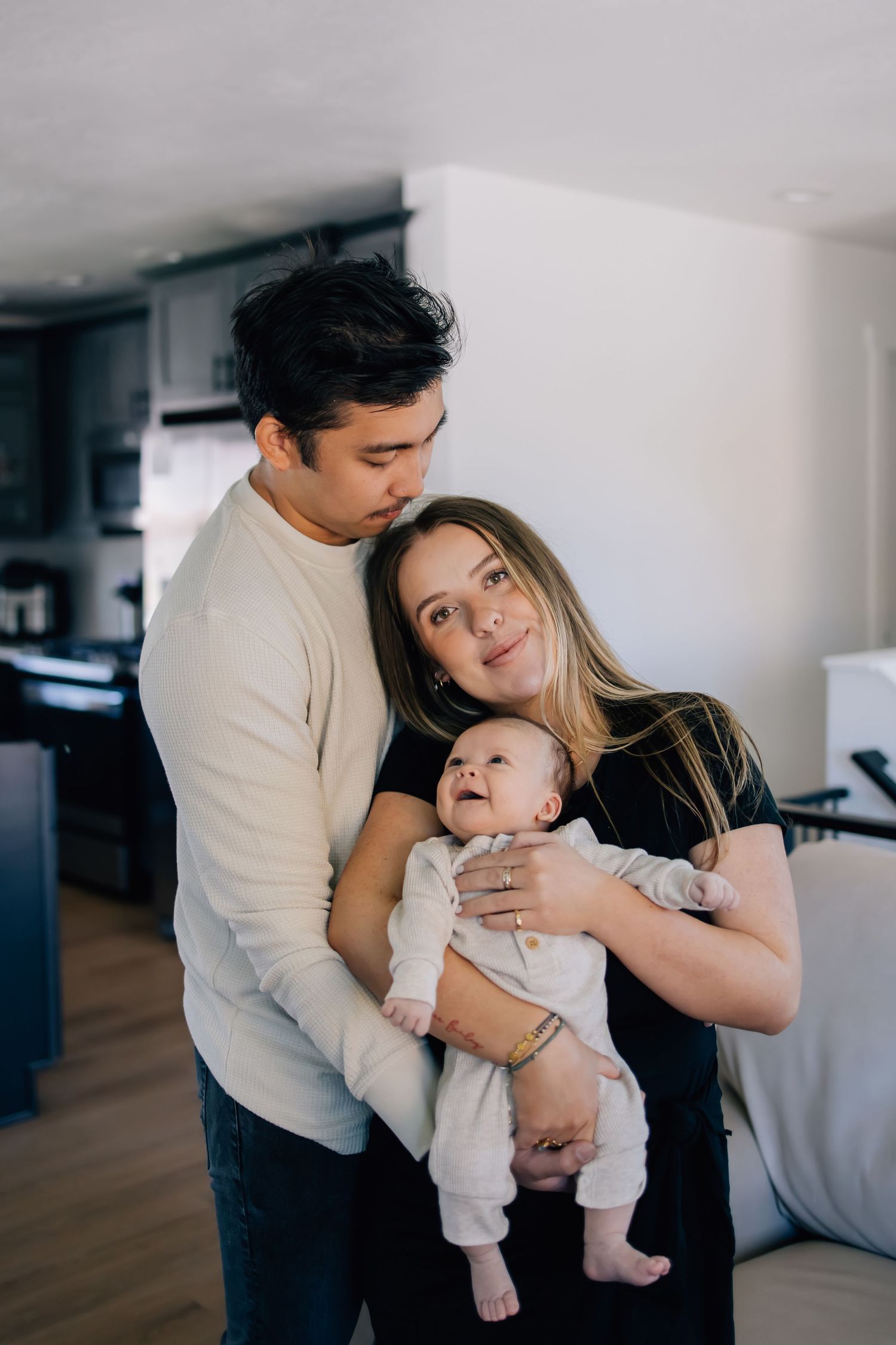 In-home lifestyle newborn photography in Salt Lake City featuring a mother holding her baby in her home surrounded by her husband as well