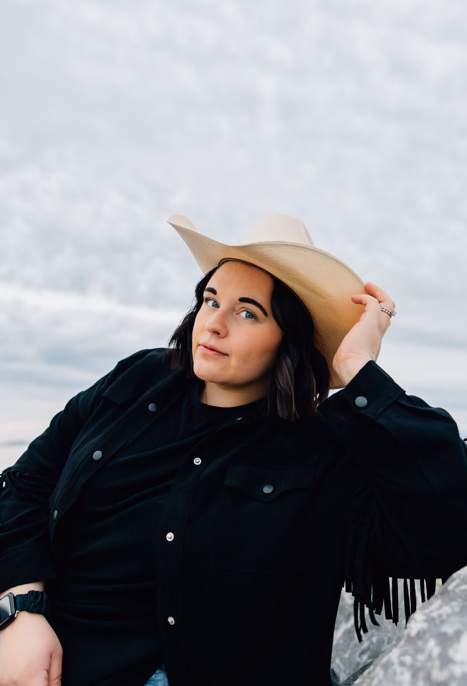 Portrait of a woman with dark brown hair in a cowgirl hat and fringe jacket