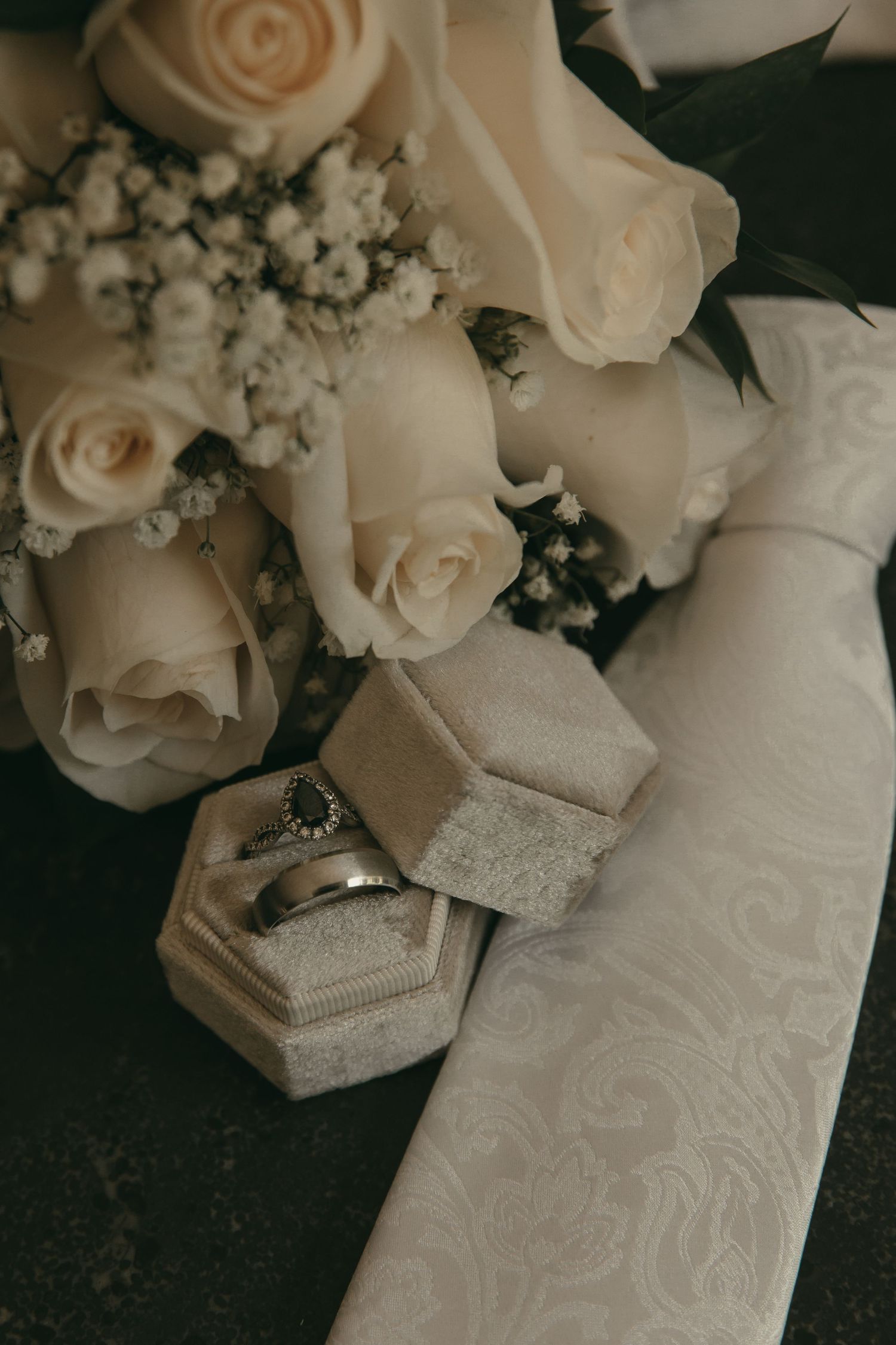Wedding details featuring white roses, wedding rings, and lace fabric flat lay in Tallmadge Ohio by Gypsy Lens Photography. Moody Wedding.