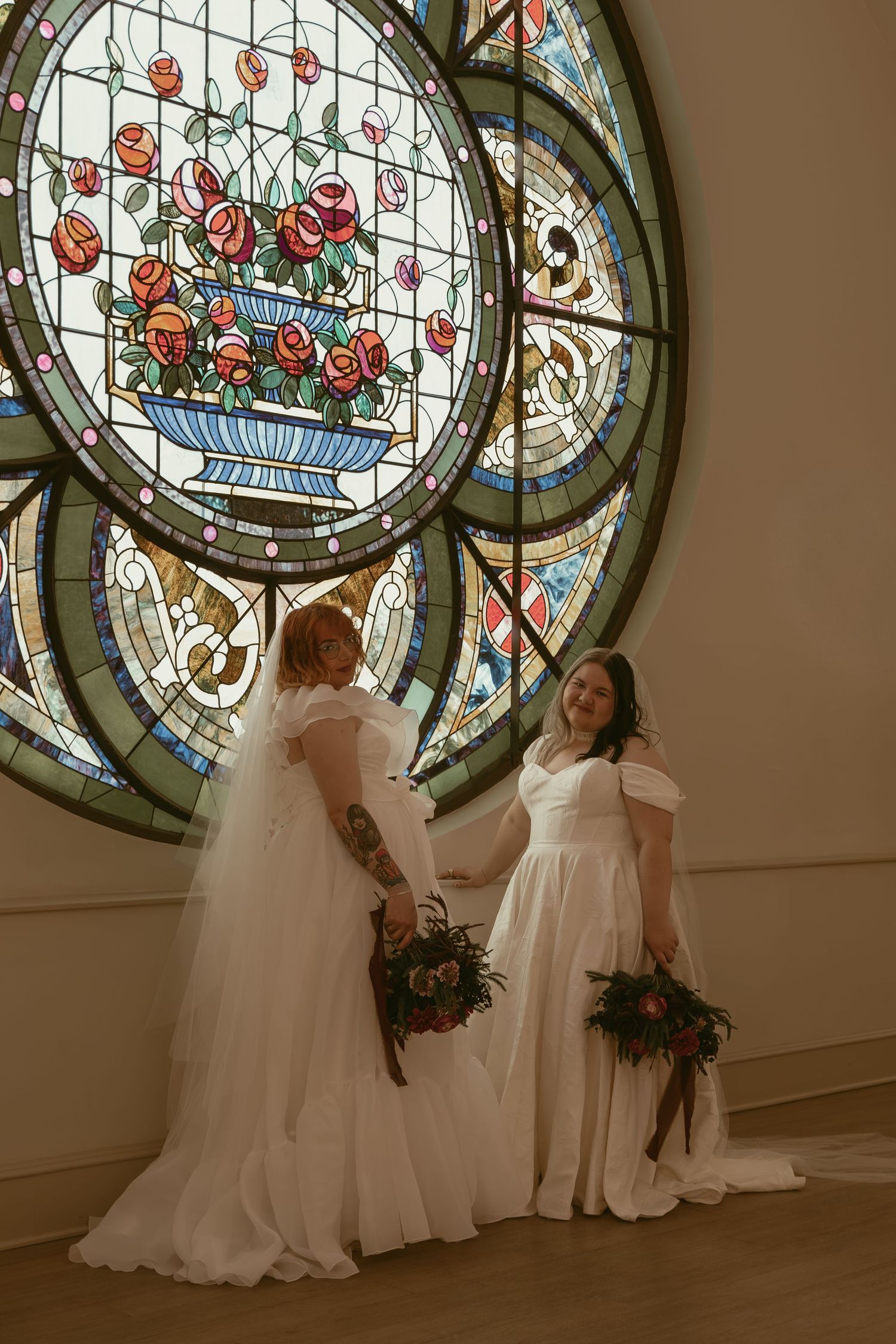 Two brides in front of stained glass in Cleveland Ohio by Gypsy Lens Photography. Moody, filmy, vintage, documentary wedding photography.