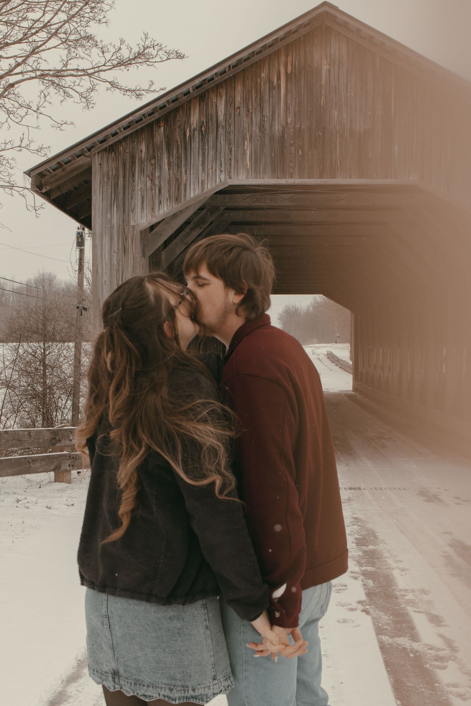 Engaged couple kissing at covered bridge in Ashtabula Ohio by Gypsy Lens Photography. Moody, vintage, documentary wedding photographer.