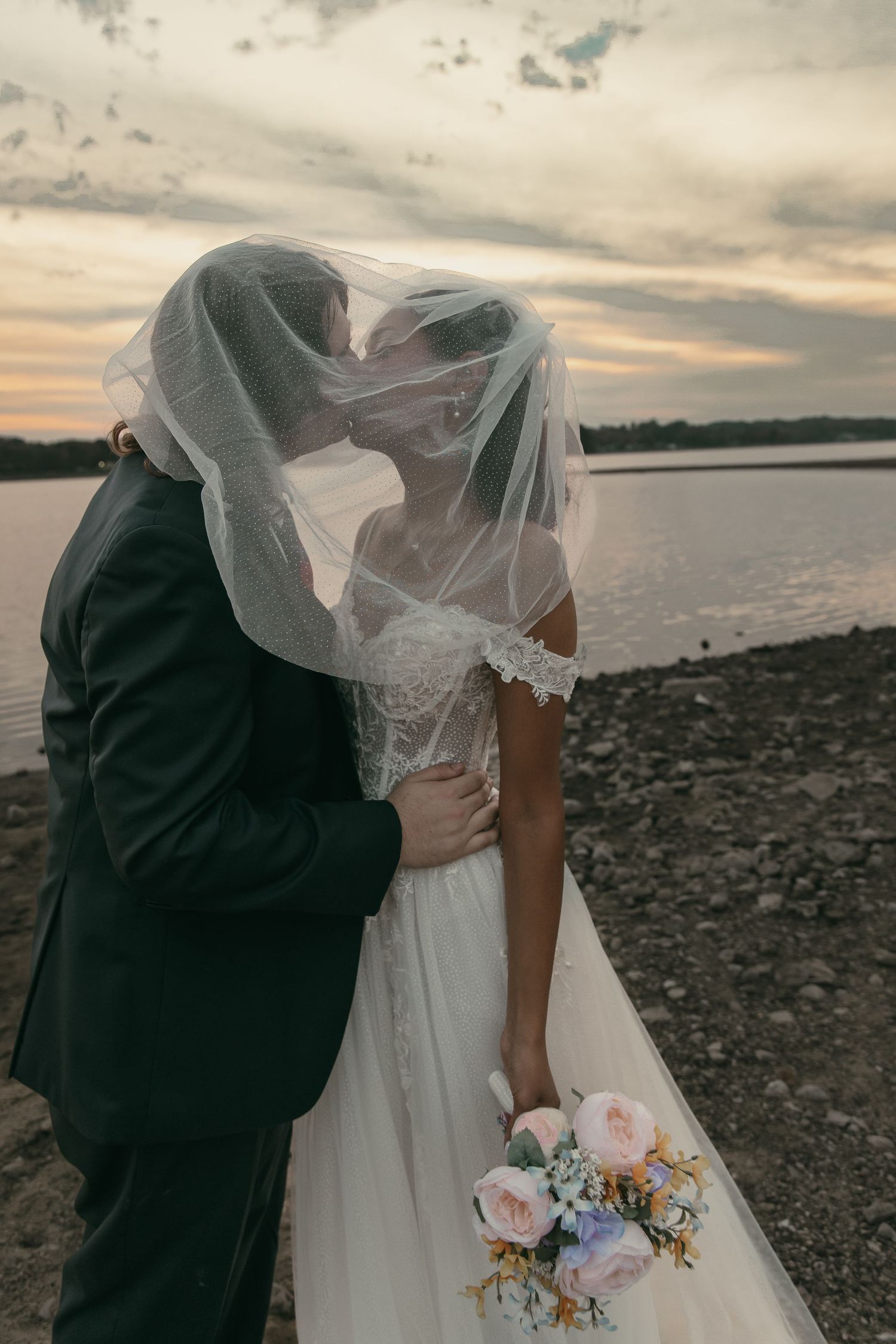 Bride and groom kissing under veil on beach in Cleveland Ohio by Gypsy Lens Photography. Moody, vintage, documentary wedding photography.