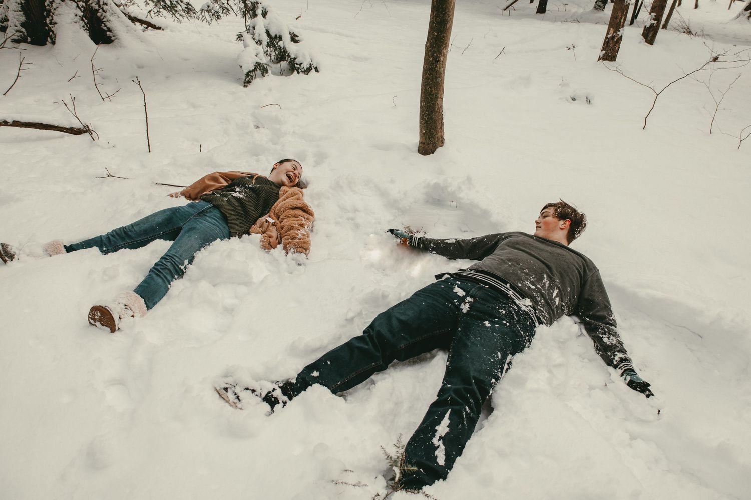 Engaged couple making snow angels in Lake County Ohio by Gypsy Lens Photography. Moody, vintage, documentary wedding photographer.