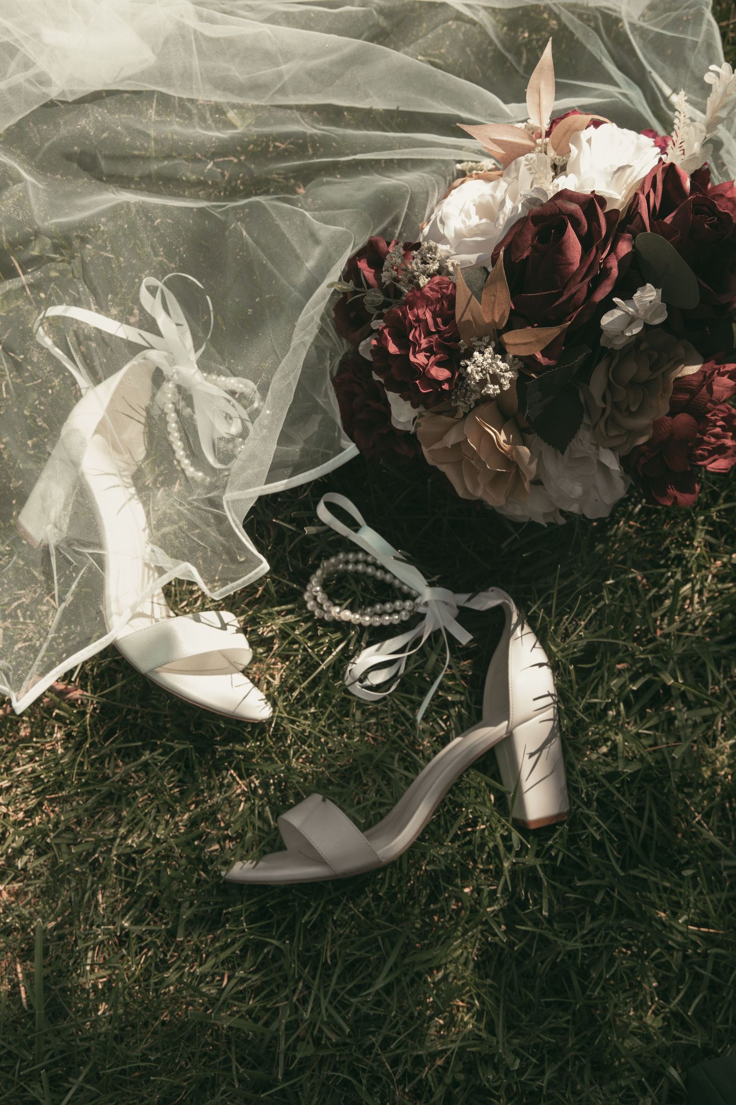 Brides shoes, bouquet, and veil in grass in Wooster Ohio by Gypsy Lens Photography. Moody, filmy, vintage, documentary wedding photography.