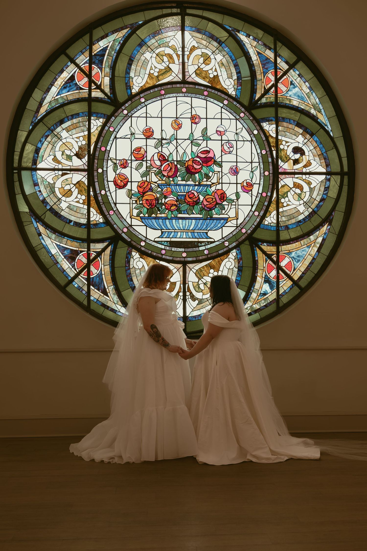 Two brides in front of stained glass in Cleveland Ohio by Gypsy Lens Photography. Moody, filmy, vintage, documentary wedding photography.