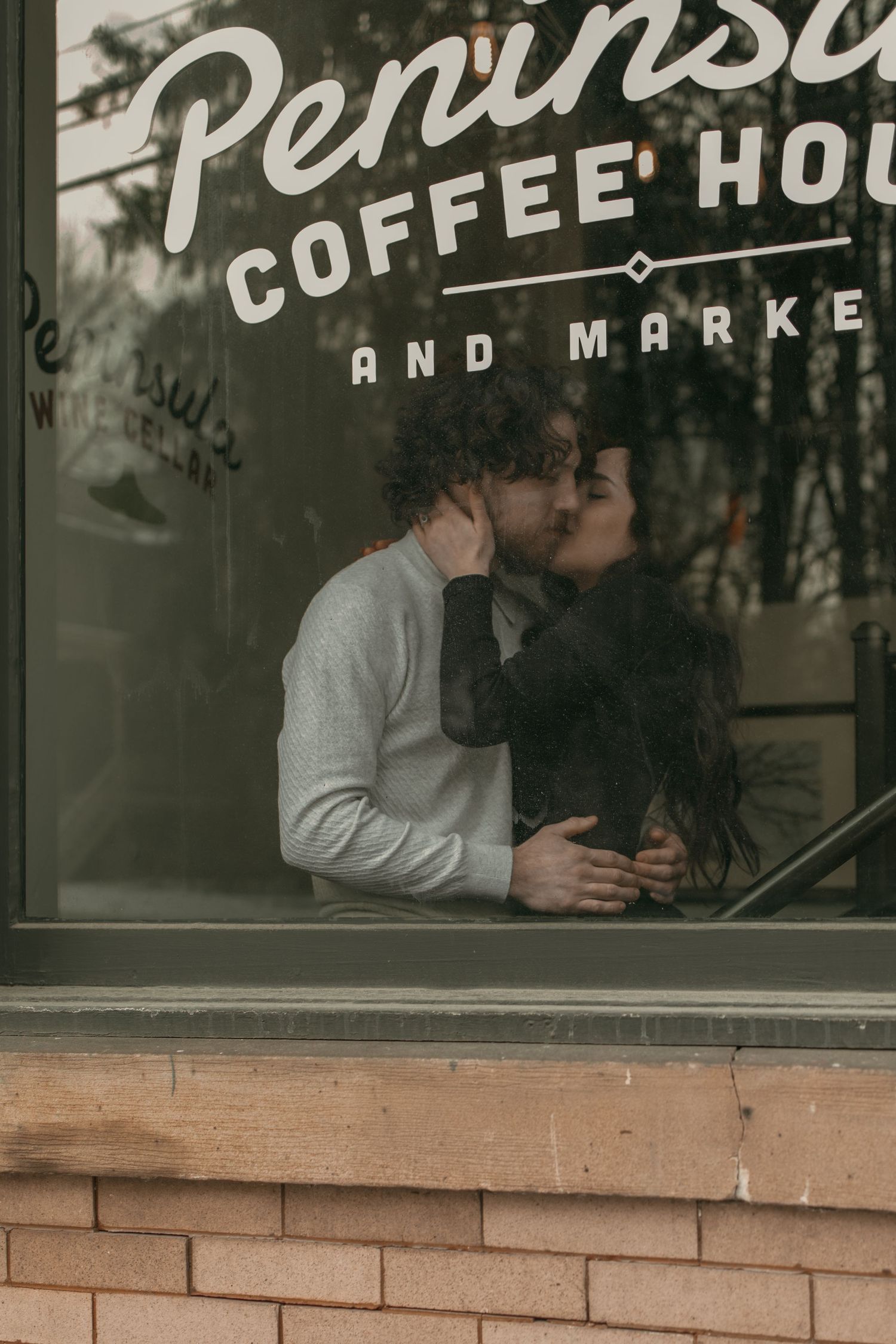 Cinematic window of engaged couple kiss in Cleveland Ohio by Gypsy Lens Photography. Moody, vintage, documentary wedding photographer.