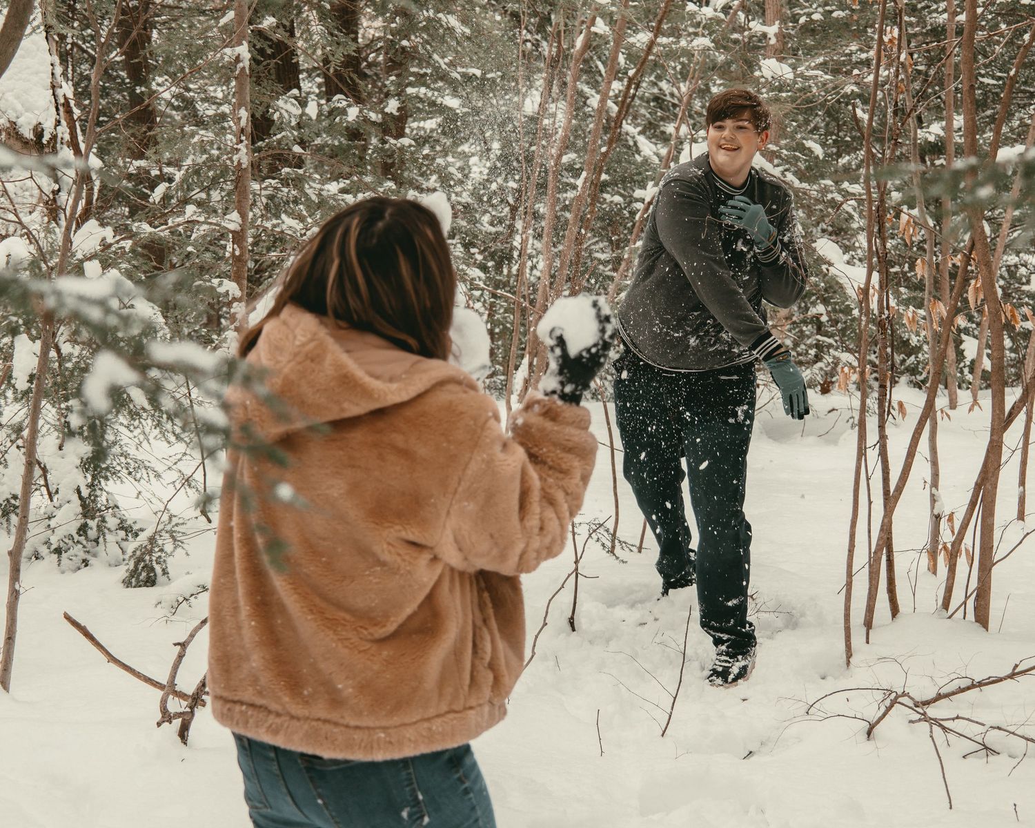 Engaged couple having snowball fight in Lake County Ohio by Gypsy Lens Photography. Moody, vintage, documentary wedding photographer.