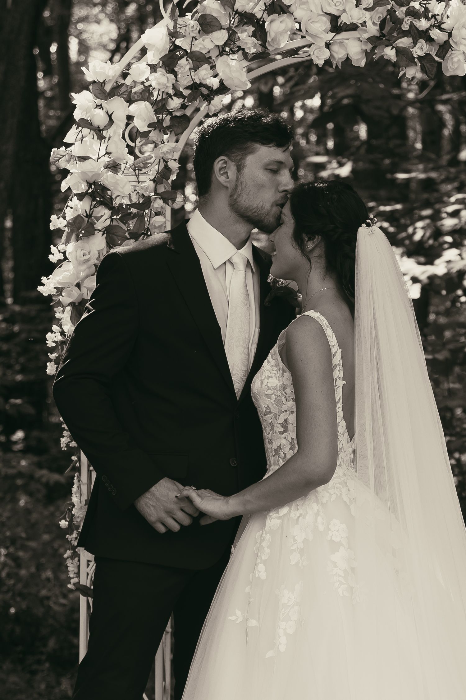 Intimate black and white wedding portrait under a floral arch in Tallmadge Ohio by Gypsy Lens Photography. Moody, documentary wedding.