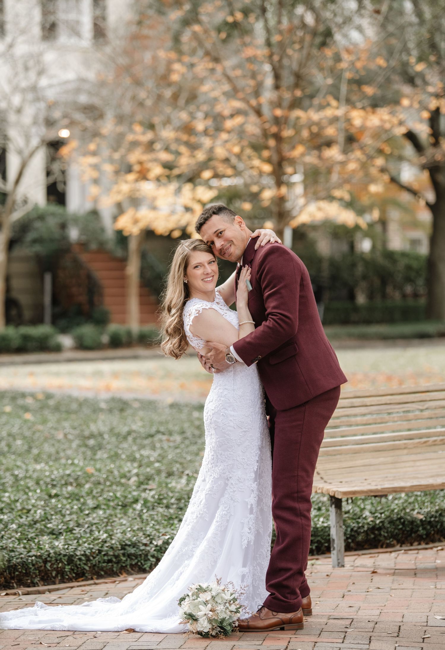 Wedding couple shares romantic moments on brick pathway surrounded by autumn trees.