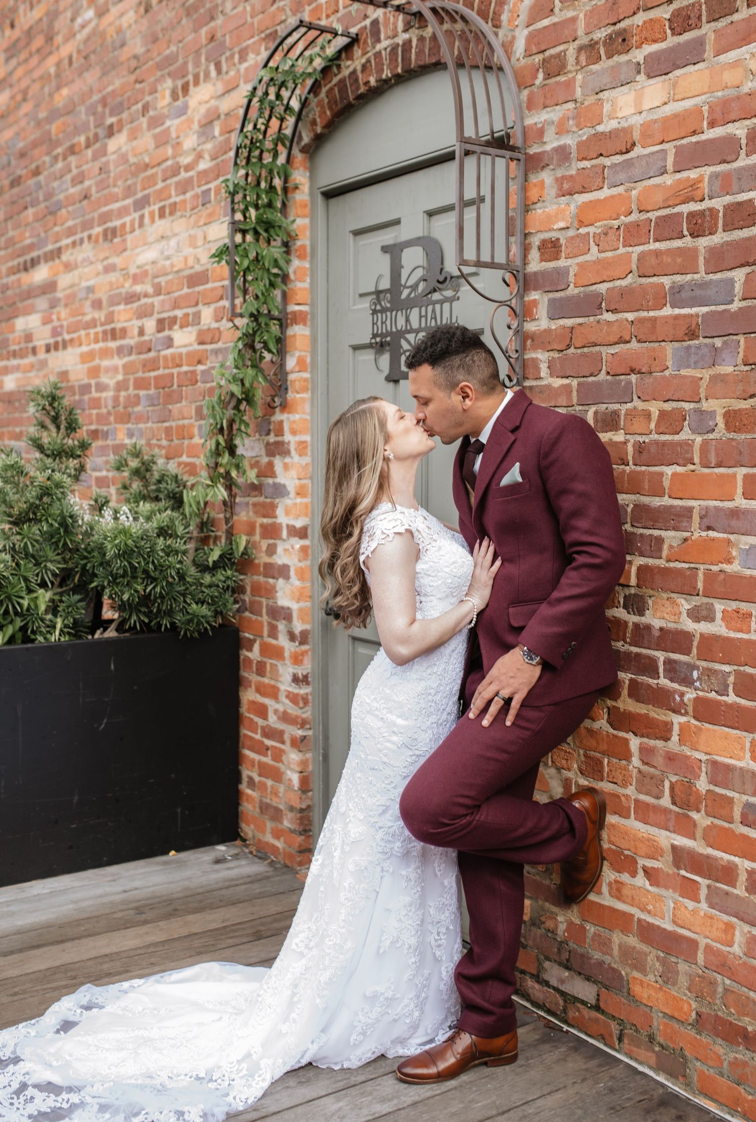 A romantic wedding moment against an exposed brick wall with burgundy and white attire.