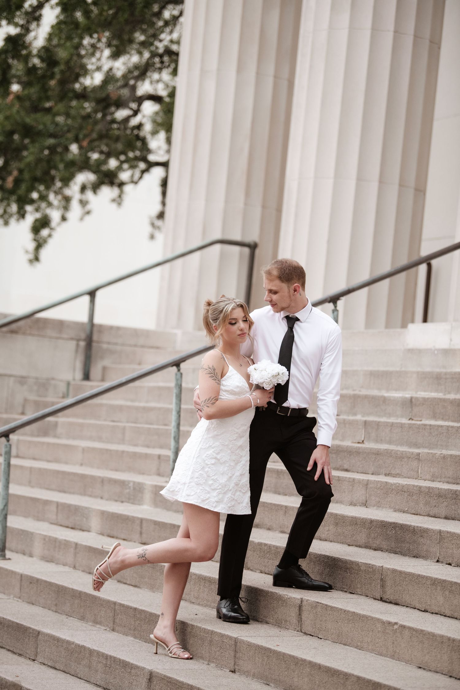 Romantic moment captured on steps of neoclassical building with columns.