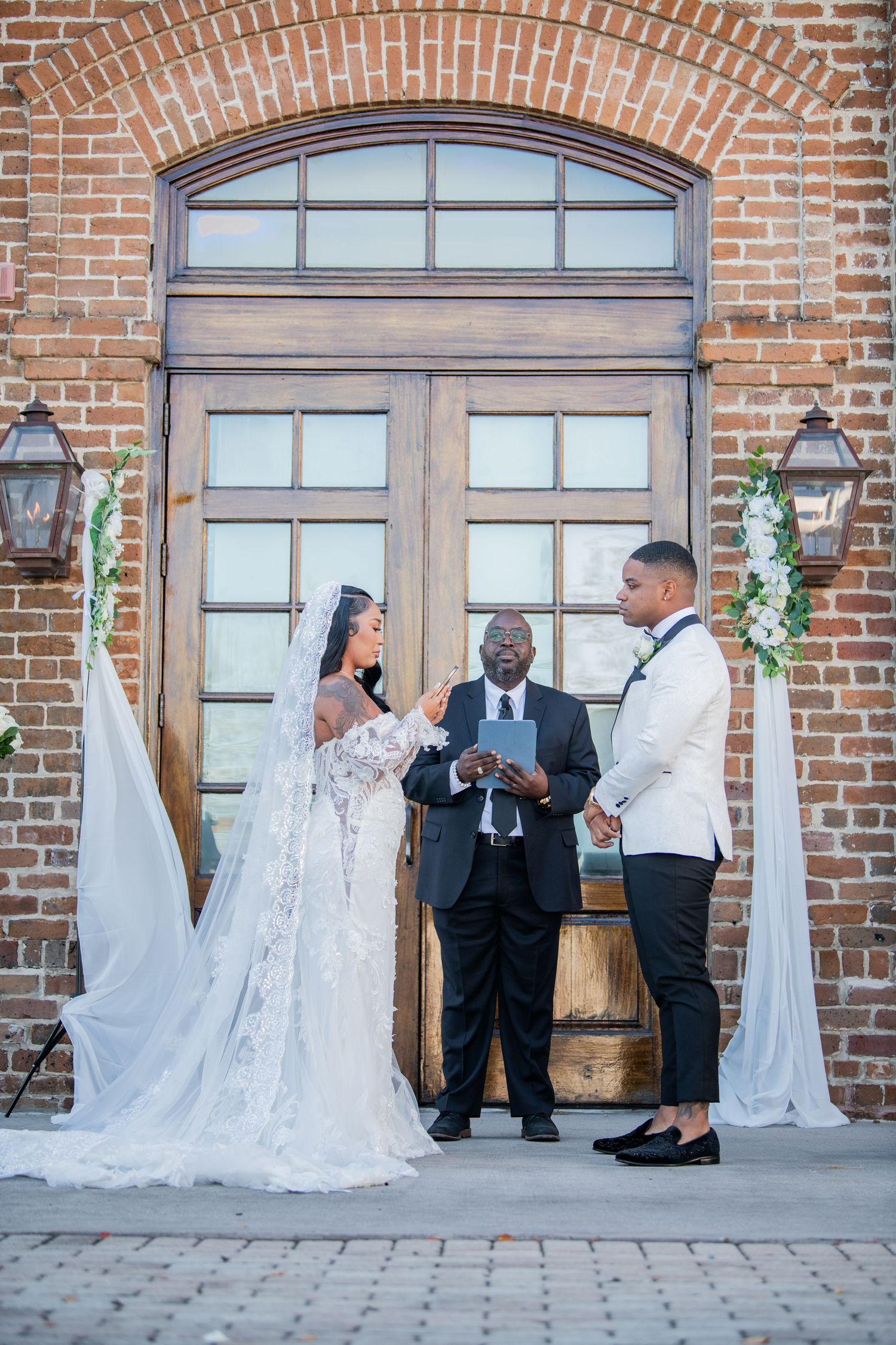 Wedding ceremony taking place outside historic brick building with arched windows.