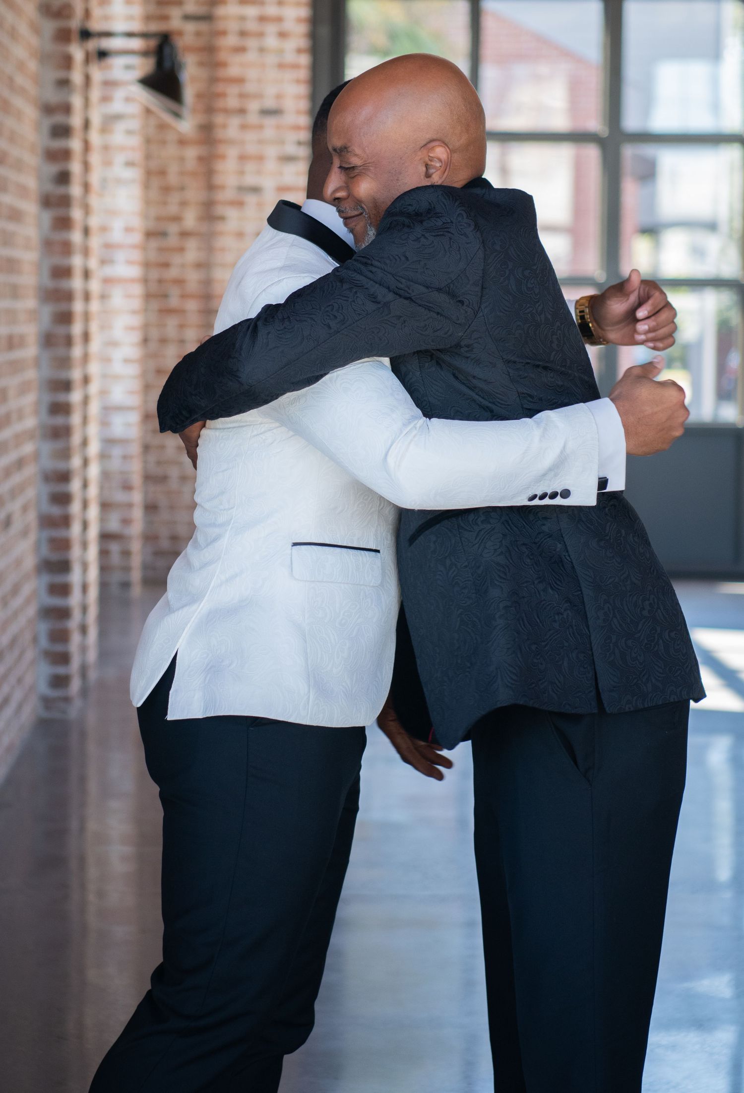 Candid moments of embraces between two people in formal attire against exposed brick walls.