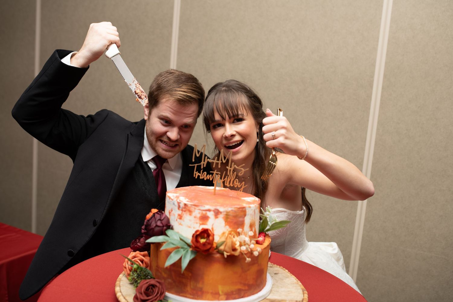 A playful cake cutting moment at a wedding reception with an orange decorated cake.