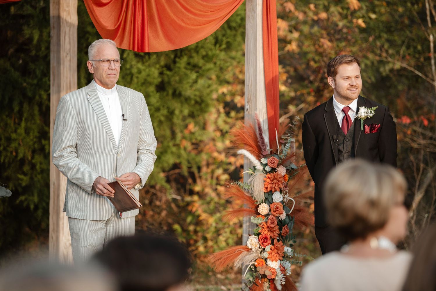 Wedding ceremony setup with orange draping and floral arrangements under trees.
