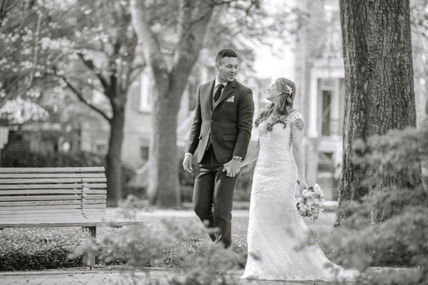 A wedding party poses for black and white portraits in a garden setting with trees and architecture.