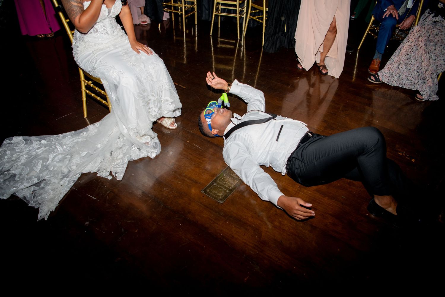 Wedding guests dance on wooden floor during reception celebration.