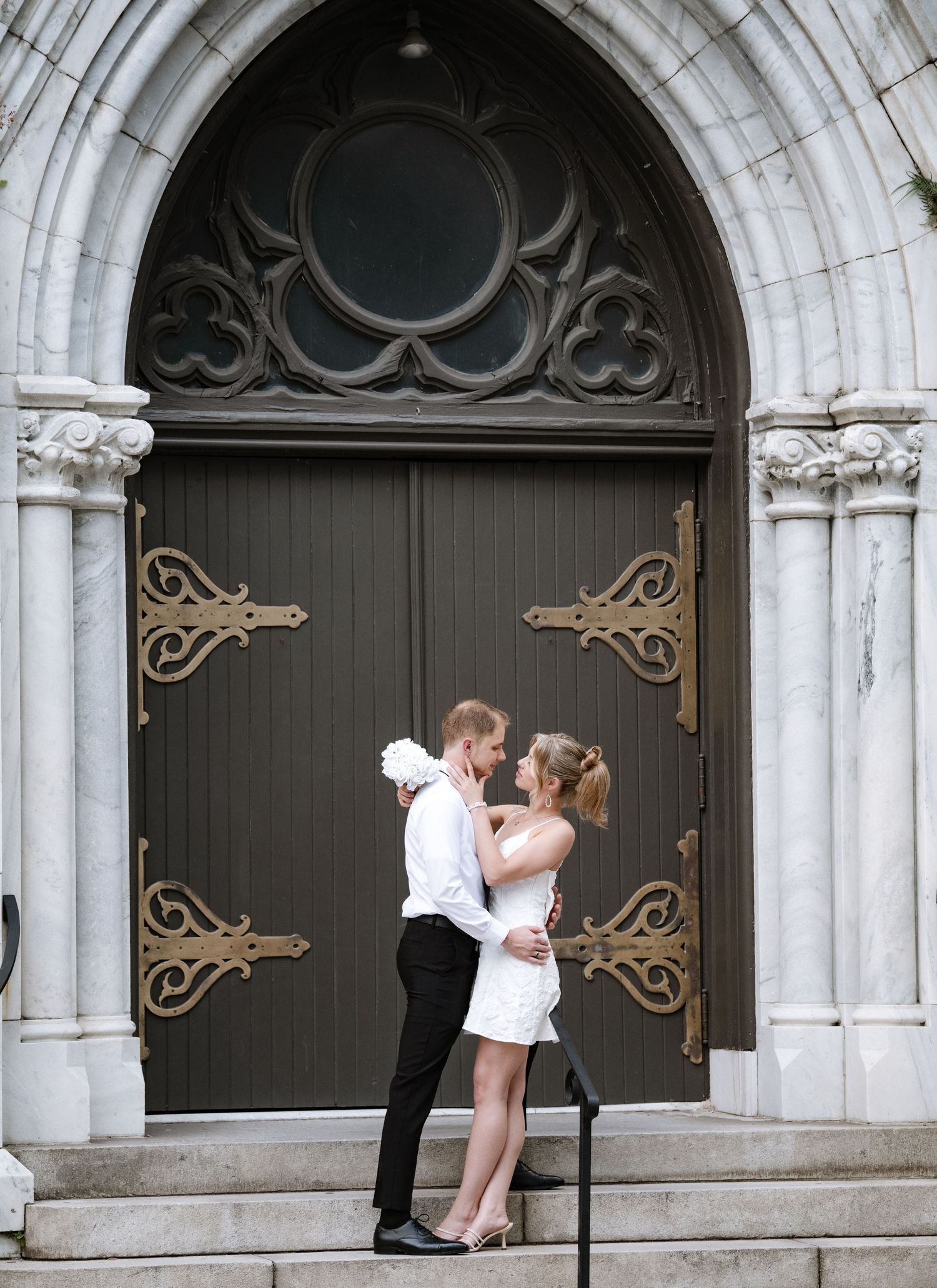 A romantic pose on church steps with an architectural arched doorway backdrop.