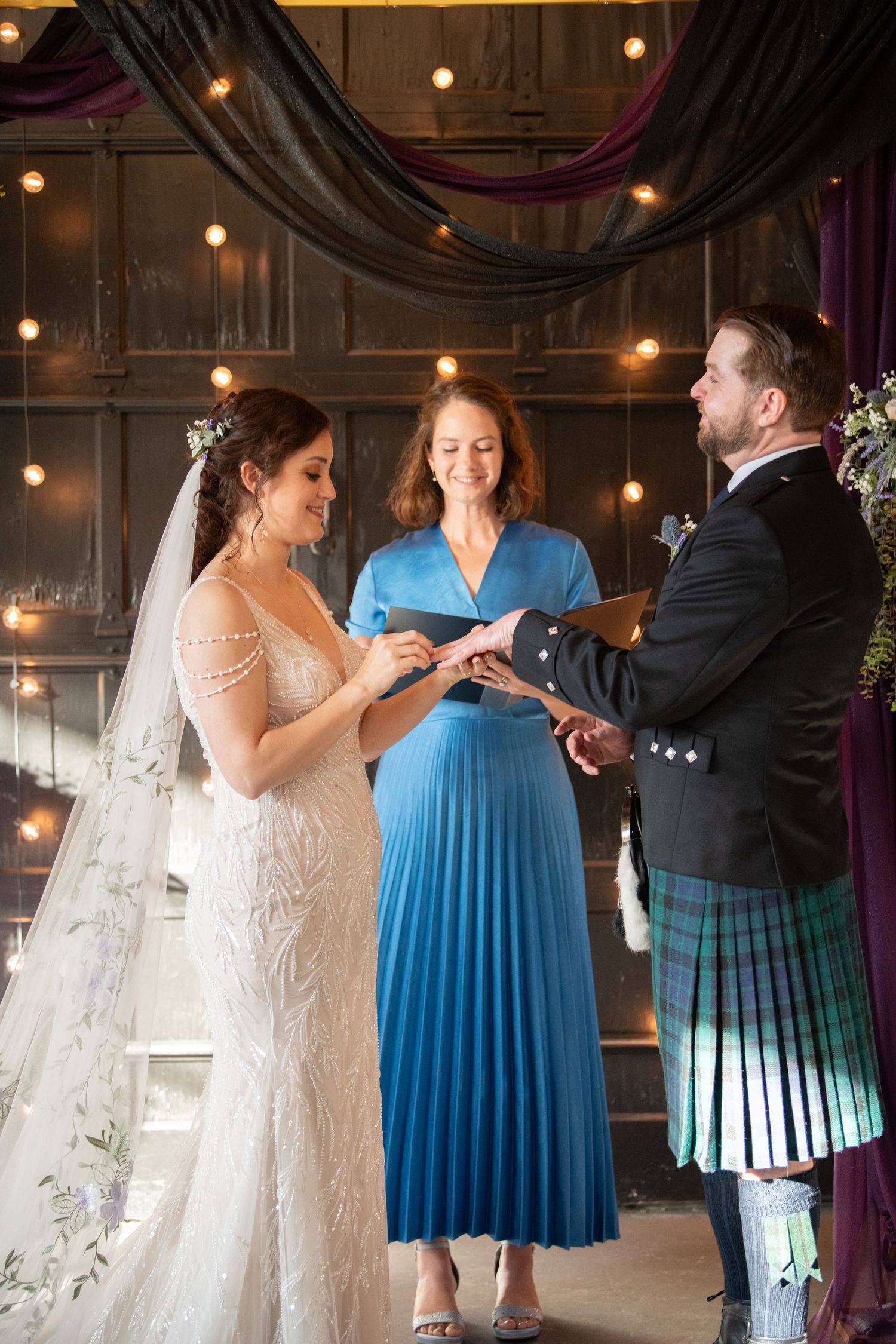 Wedding ceremony with bride in lace gown and groom in kilt exchanging vows.